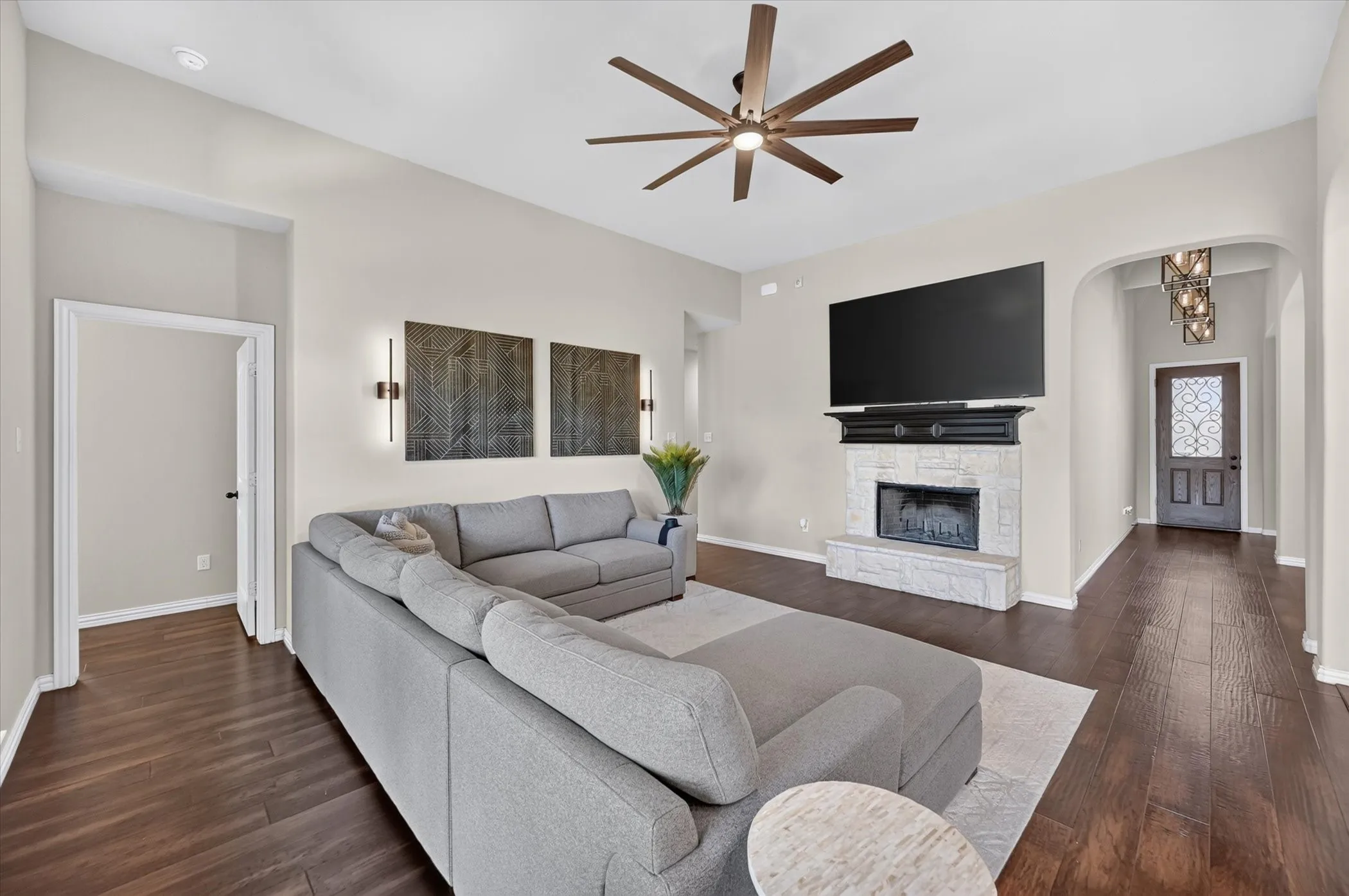 Spacious open-concept living area featuring a large sectional arrangement, wood-finish flooring throughout, and a contemporary ceiling fan with brushed metal accents