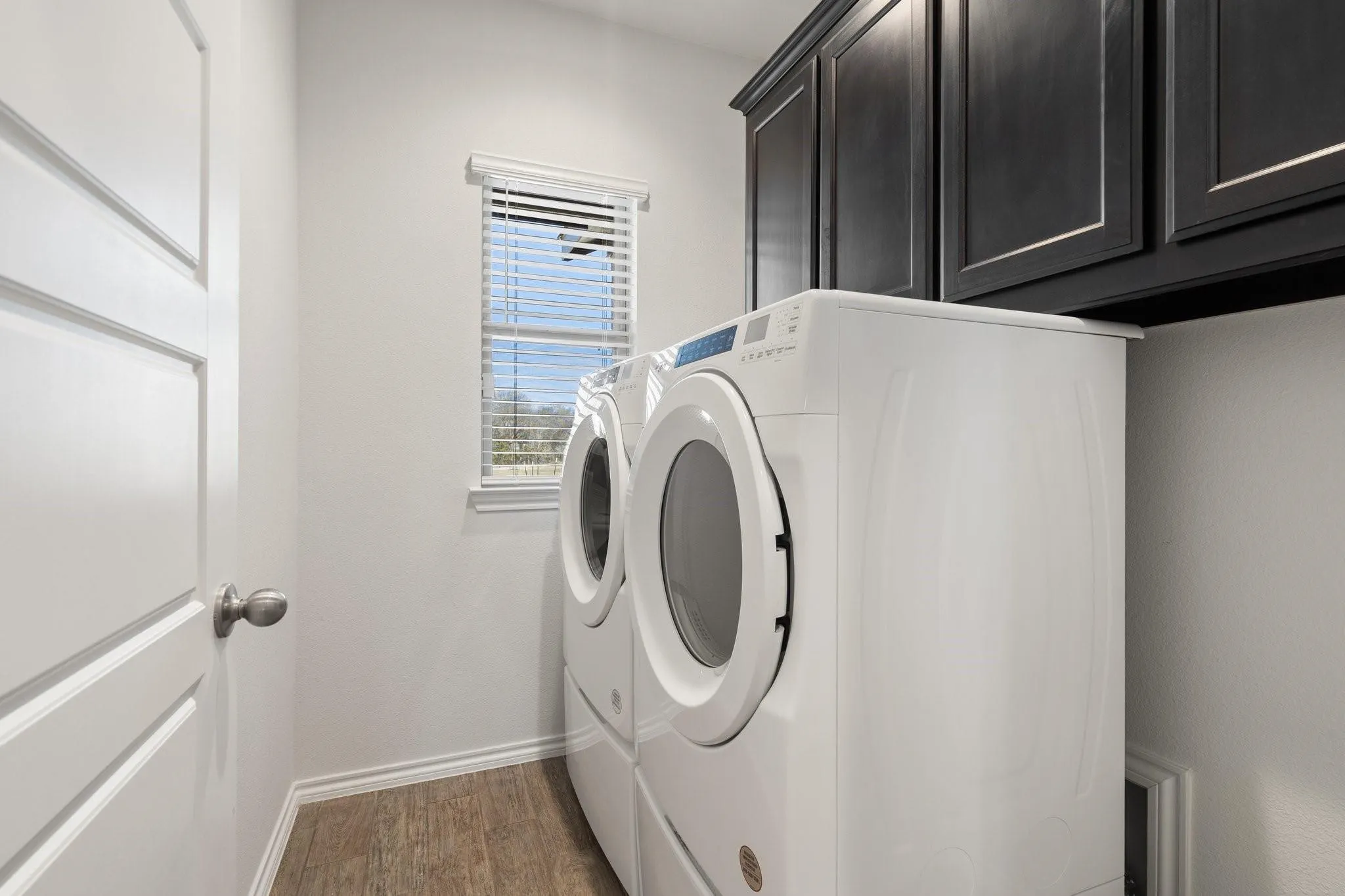 Washroom with cabinet space, wood finished floors, washing machine and clothes dryer, and baseboards