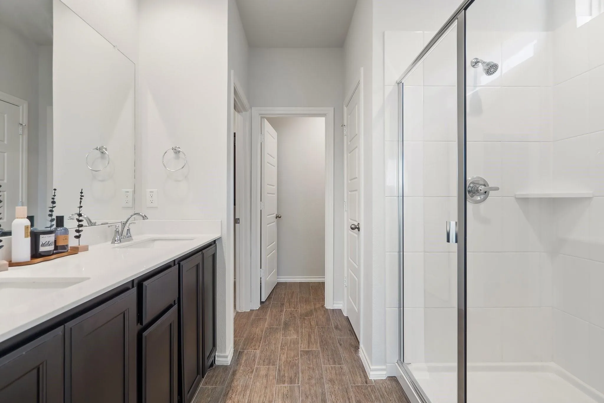 Bathroom with double vanity, wood finished floors, a sink, baseboards, and a stall shower