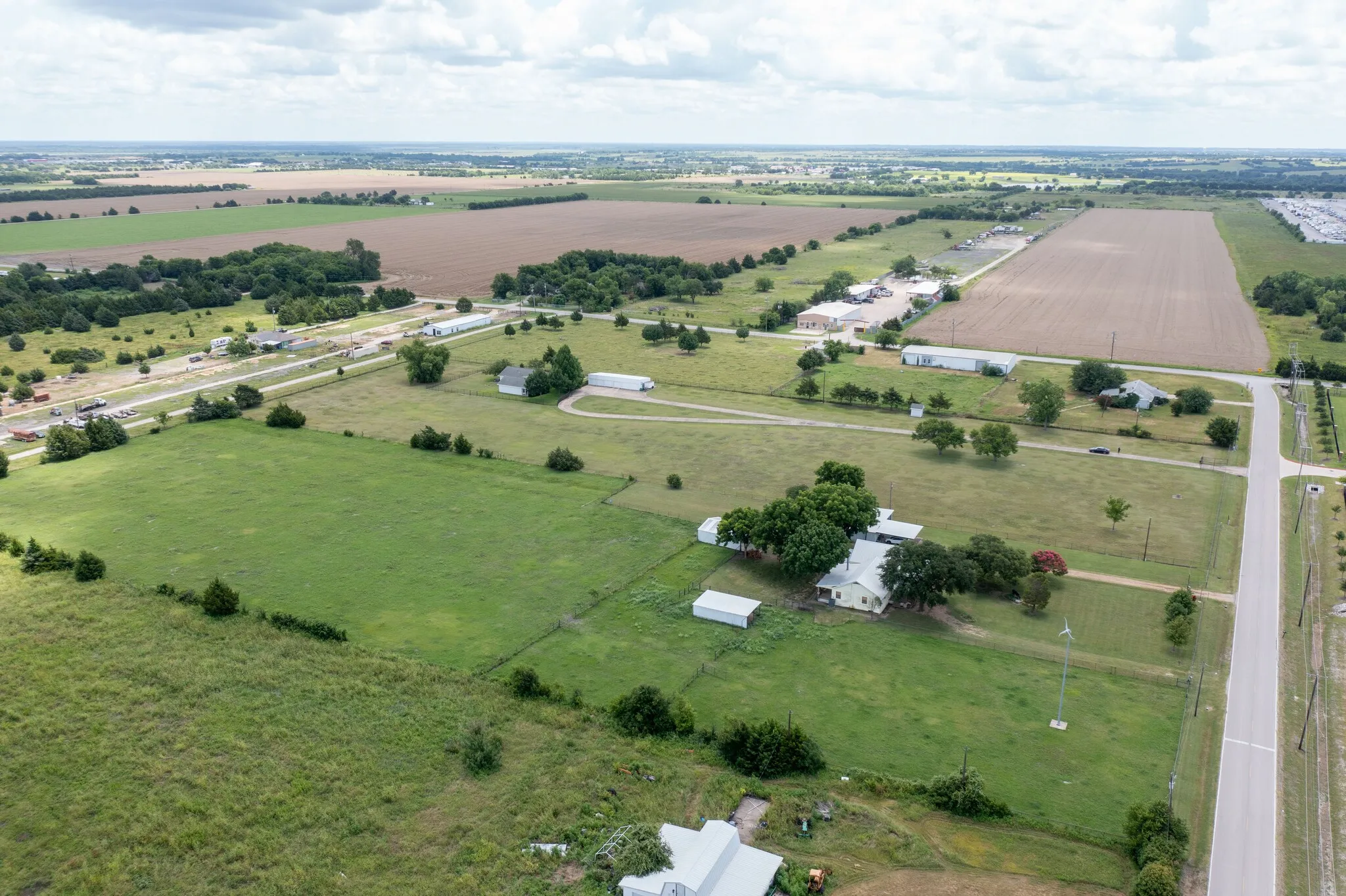 Expansive land parcel featuring open fields, scattered mature trees, and multiple outbuildings