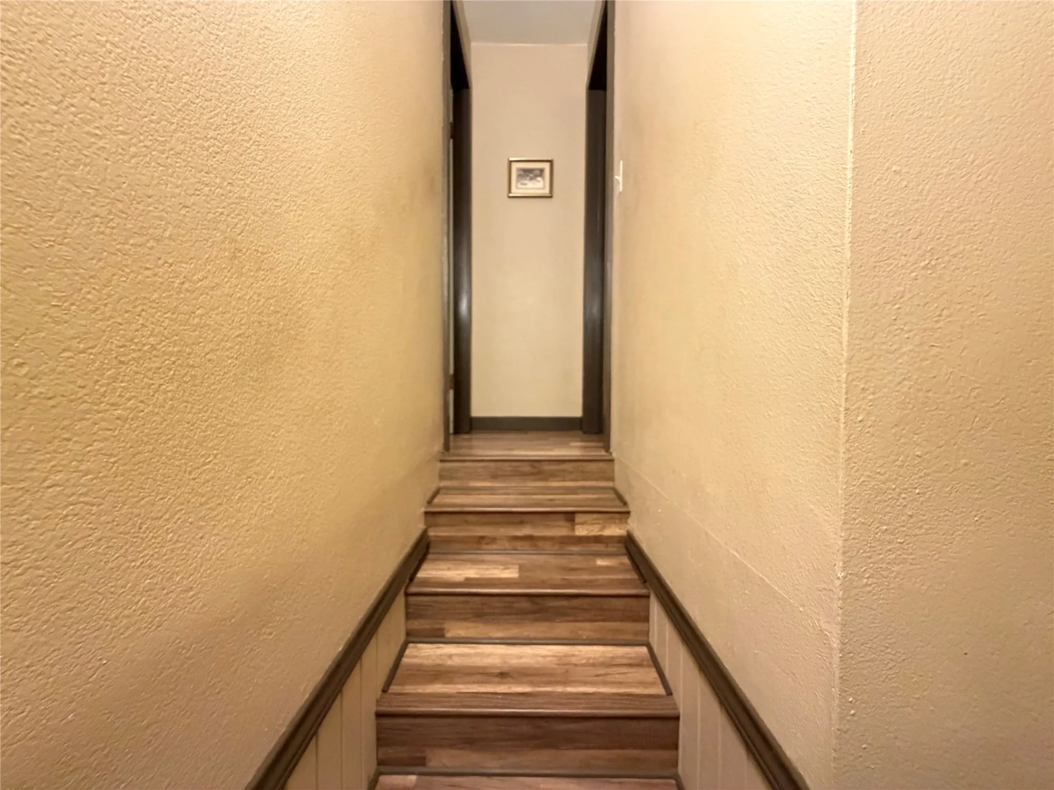 Staircase featuring wood-finish treads and risers, textured walls, and dark trim