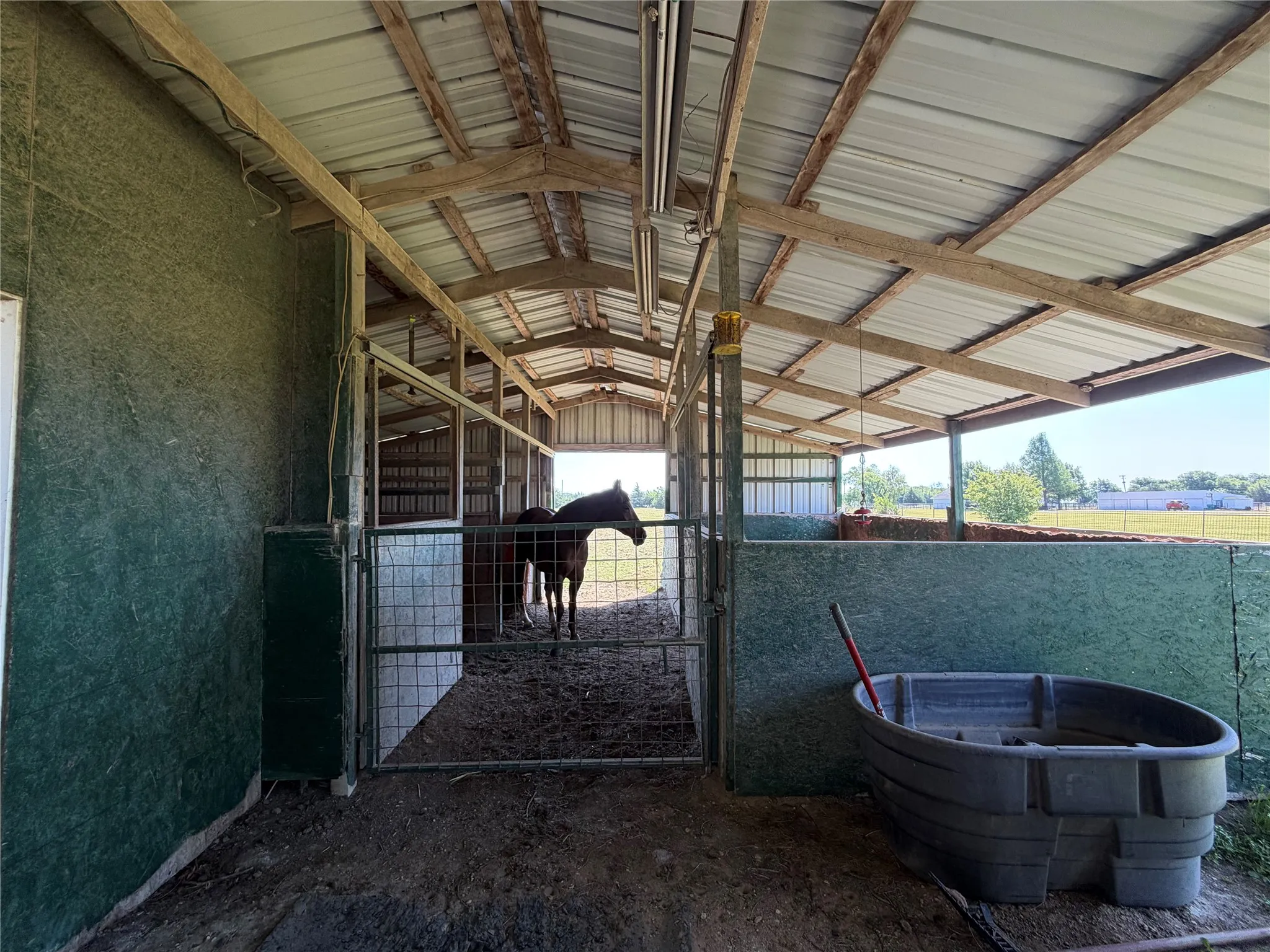 Metal roof barn structure with exposed wood beams and enclosed stalls featuring metal gates