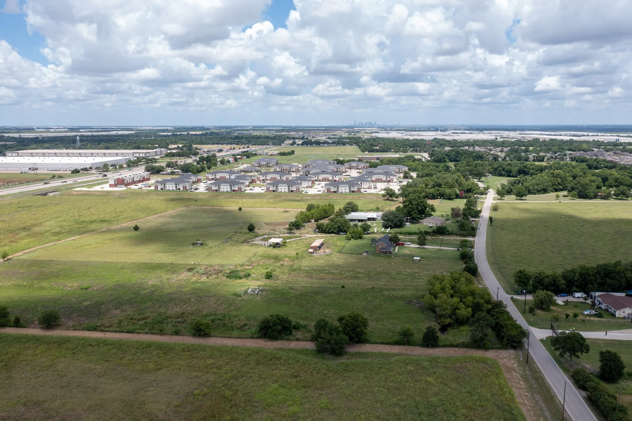Expansive open land with established roadways, mature trees, and nearby residential developments