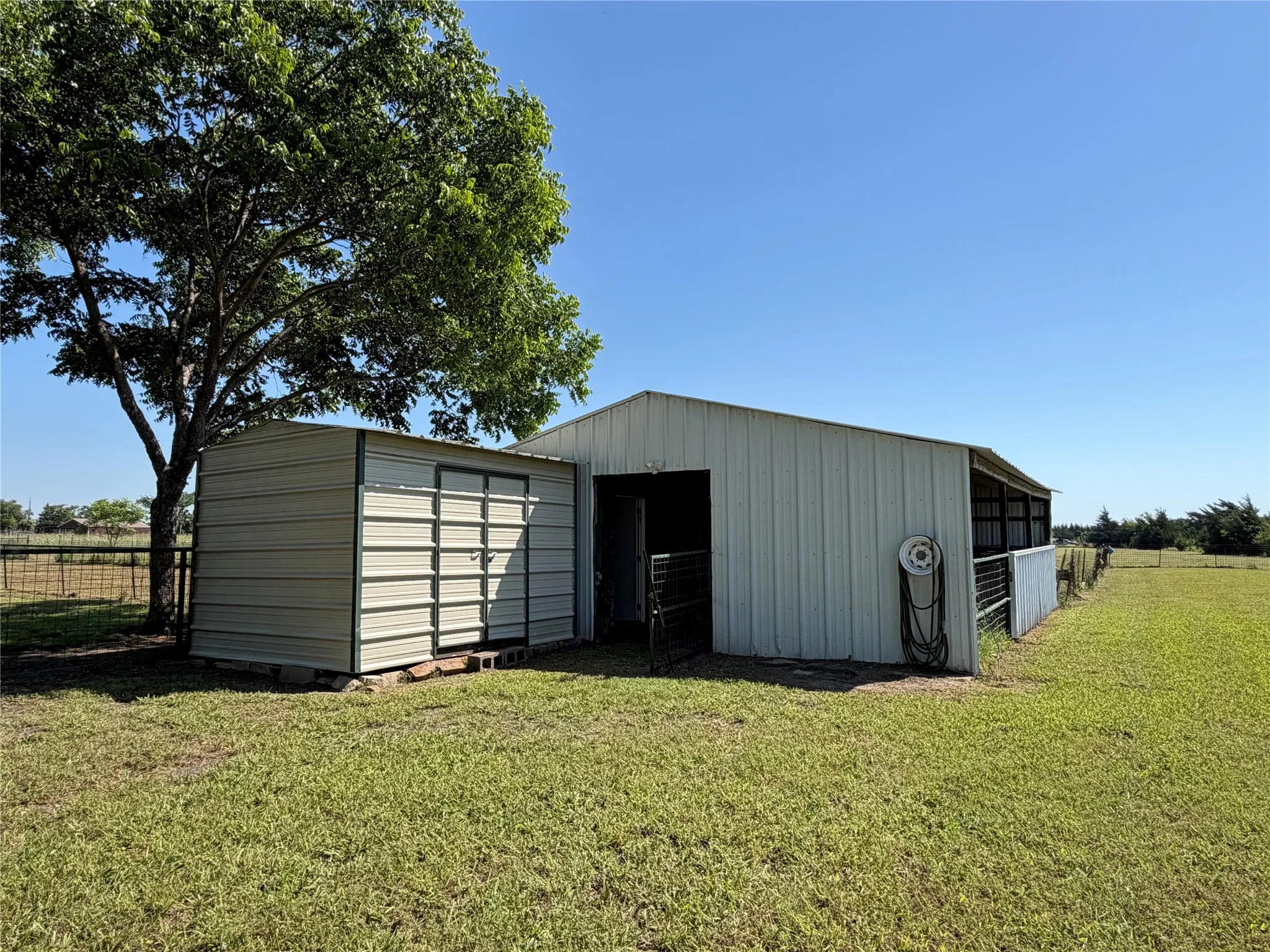 Metal outbuilding with attached open-sided structure and a separate metal shed, situated on a grassy expanse