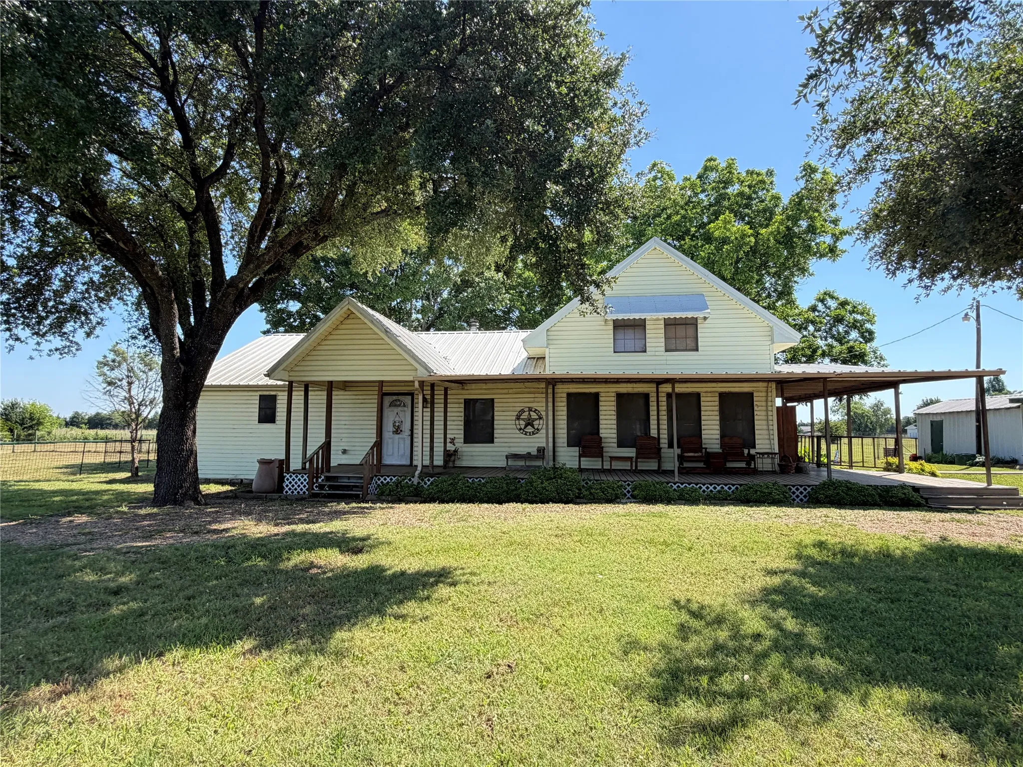 Siding exterior with a metal roof, extended covered porch, covered carport, and mature trees