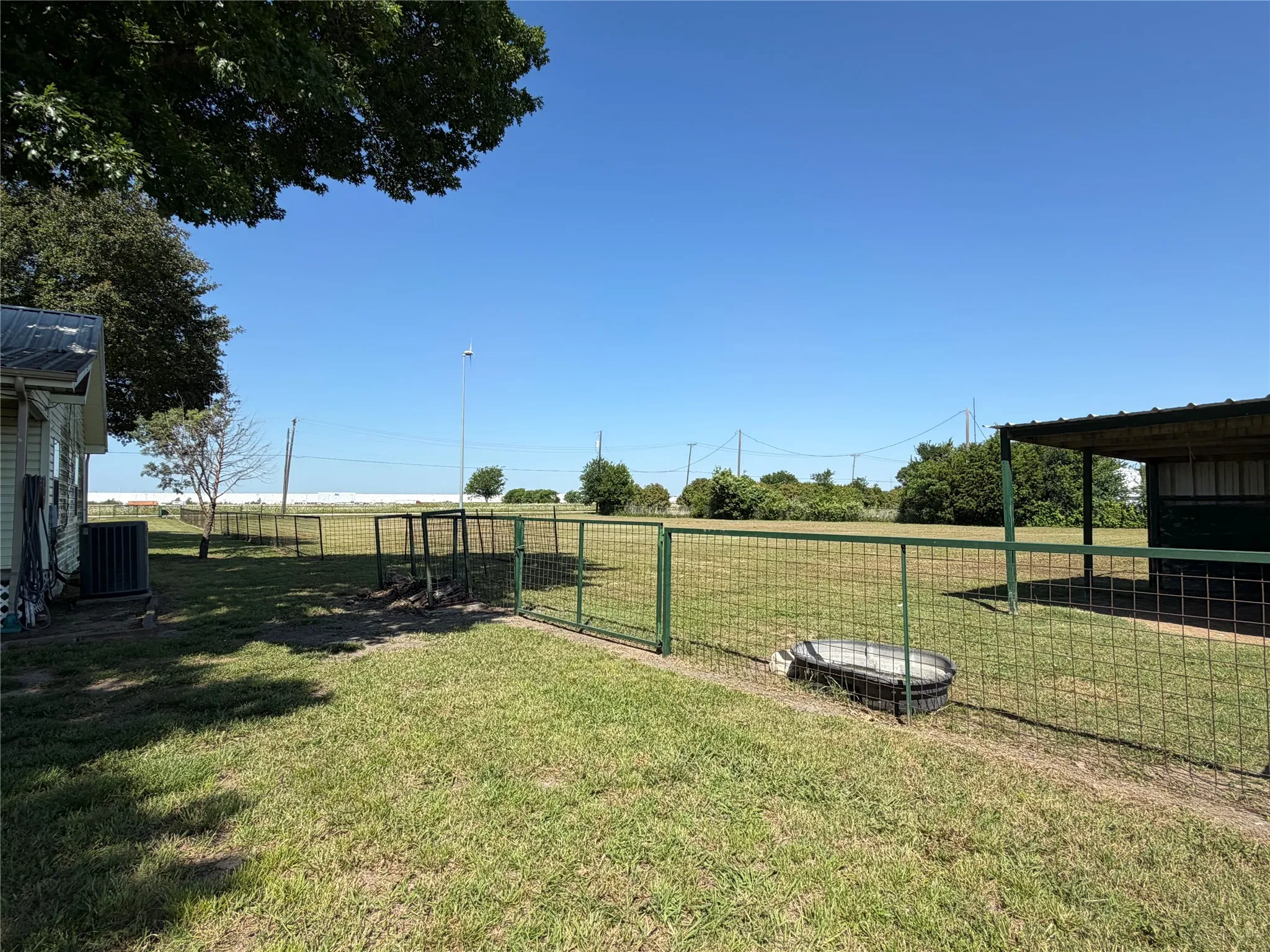Expansive grassy area with a partial metal fence and a utility structure featuring a metal roof