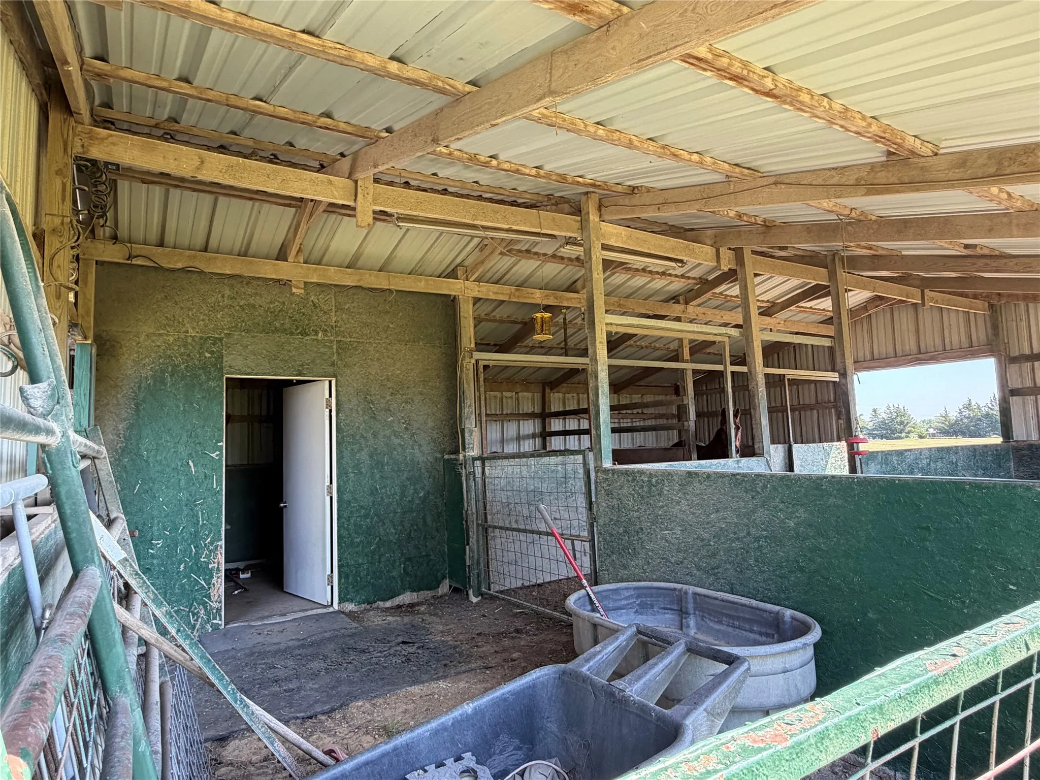 Barn structure featuring exposed wood beams, corrugated metal roofing, and green-paneled interior walls