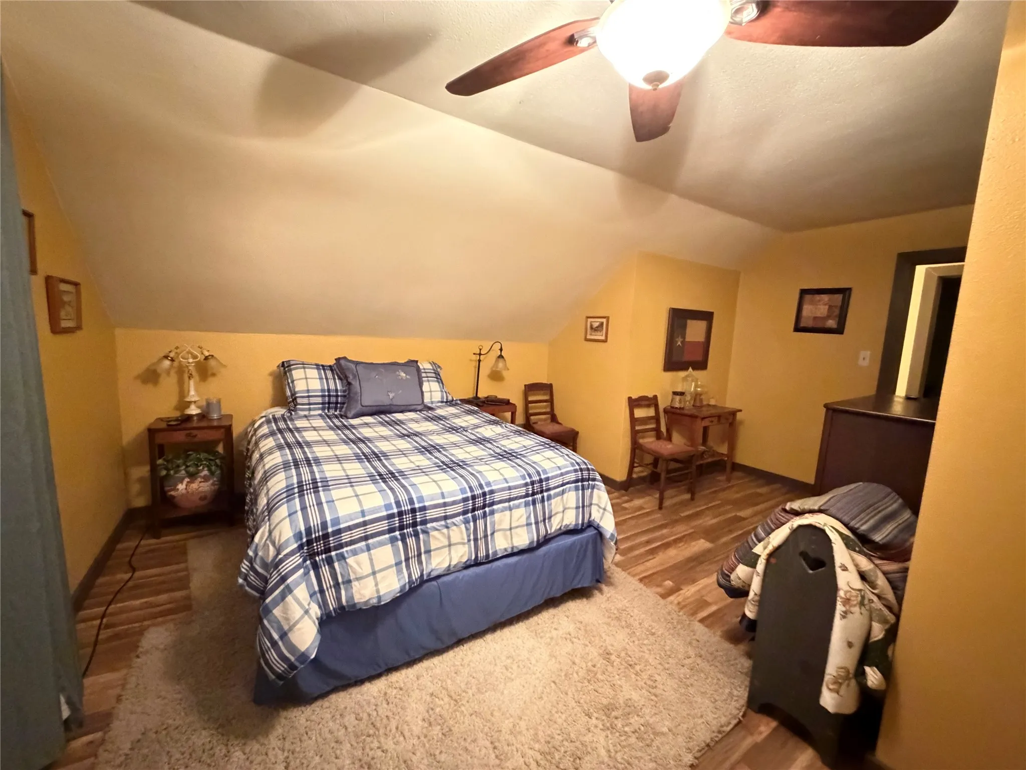 Wood-finish flooring, ceiling fan with integrated lighting, sloped ceiling, and an open doorway
