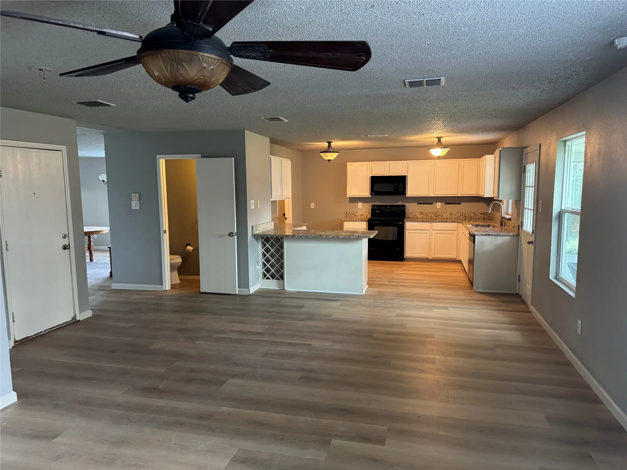 Kitchen featuring white cabinets, black appliances, light stone counters, a peninsula, and a ceiling fan