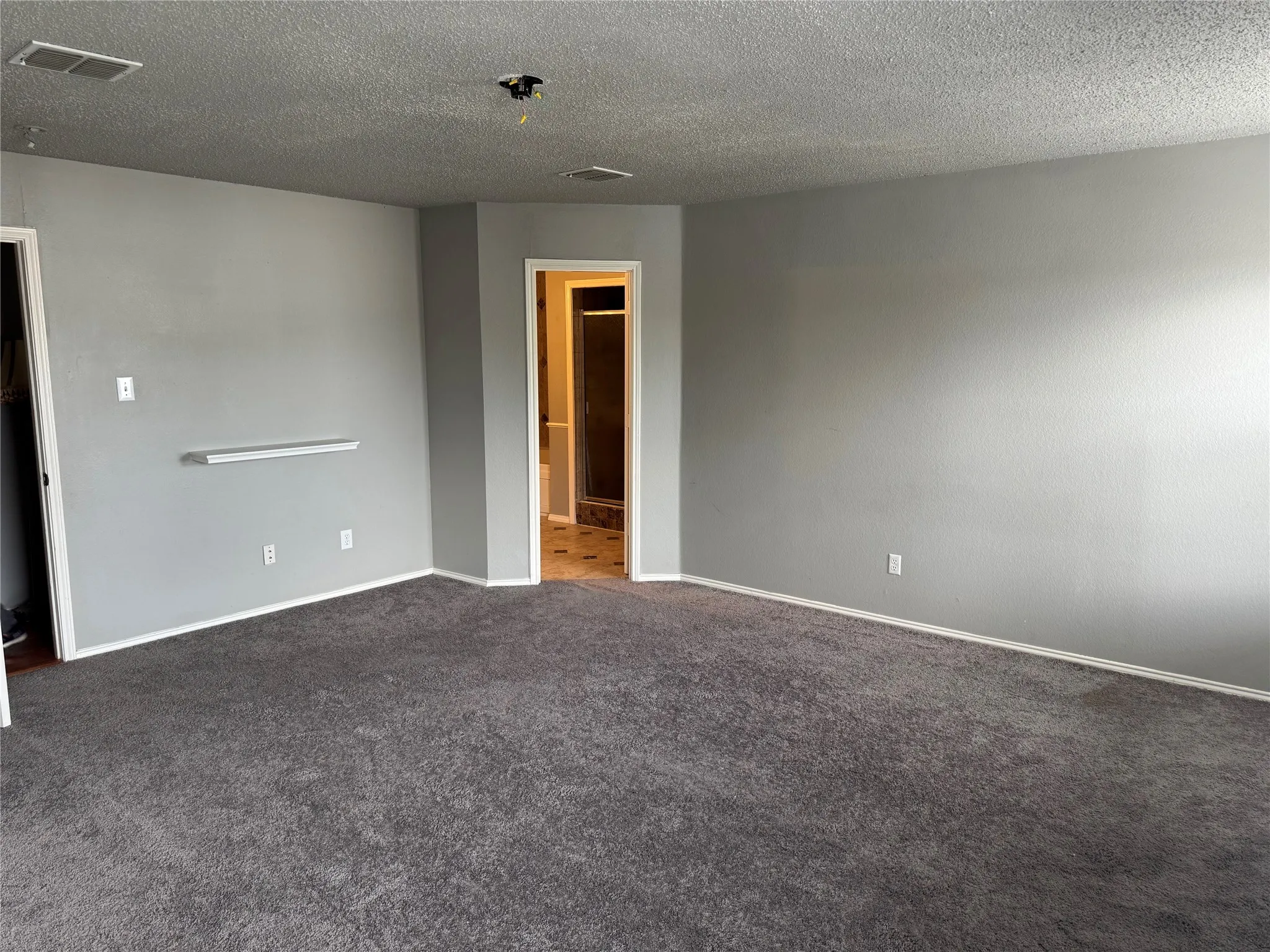 Carpeted empty room featuring a textured ceiling and baseboards