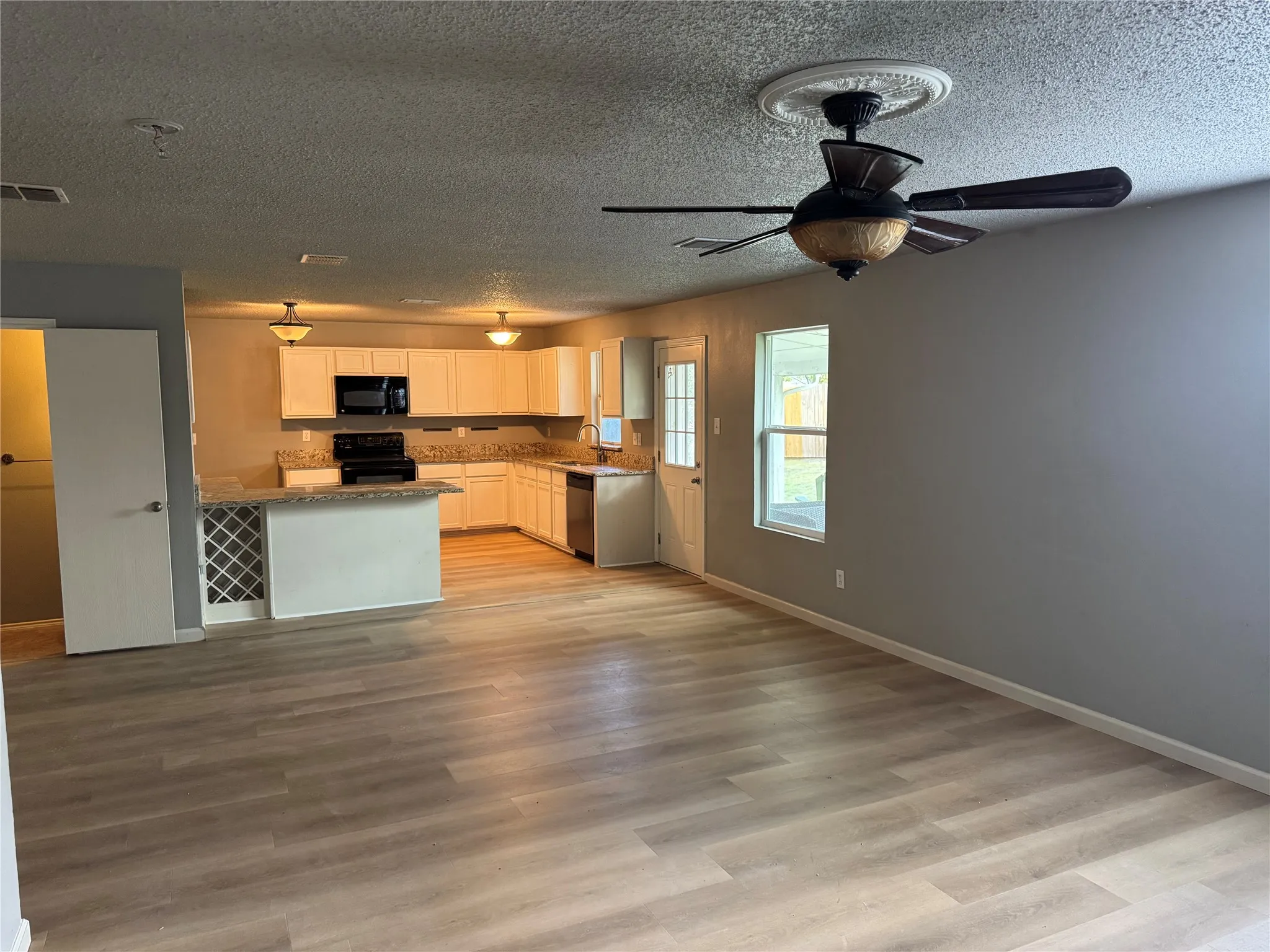 Kitchen with white cabinetry, black appliances, open floor plan, a textured ceiling, and light wood-style flooring