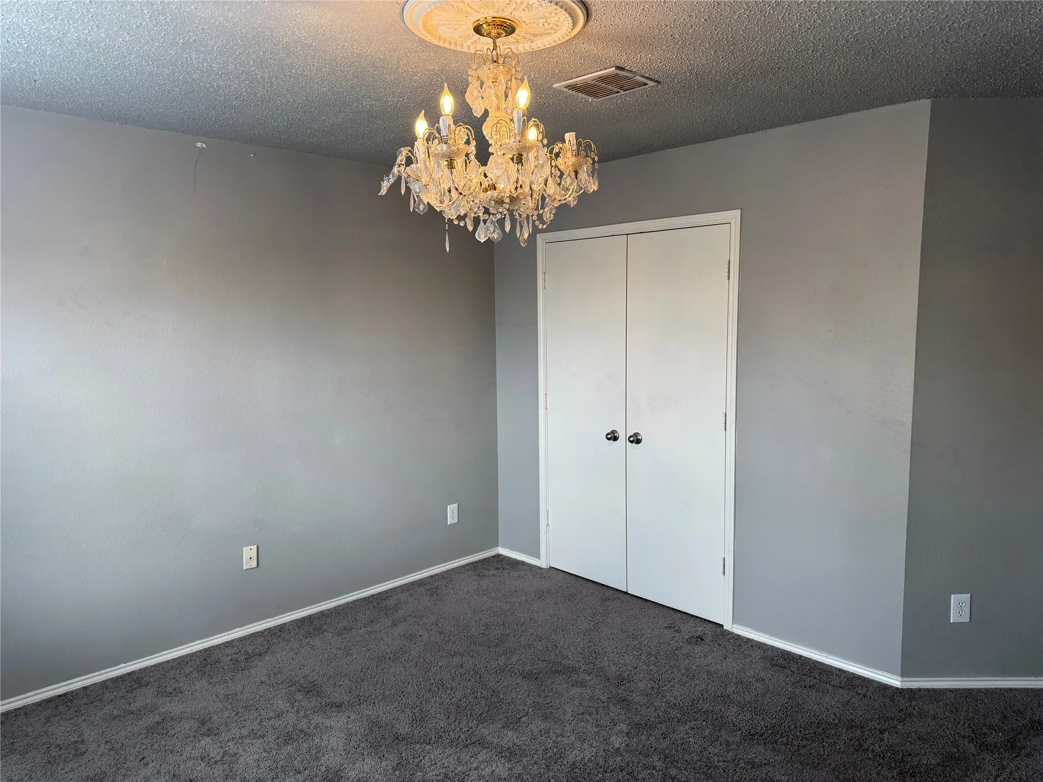 Unfurnished bedroom featuring a textured ceiling, carpet floors, a chandelier, and a closet