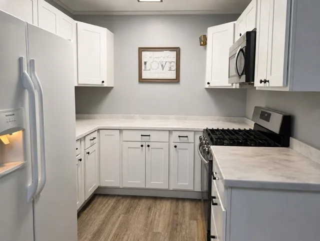 White shaker-style cabinetry with black hardware, light-toned countertops, wood-finish flooring, and a stainless steel over-the-range microwave