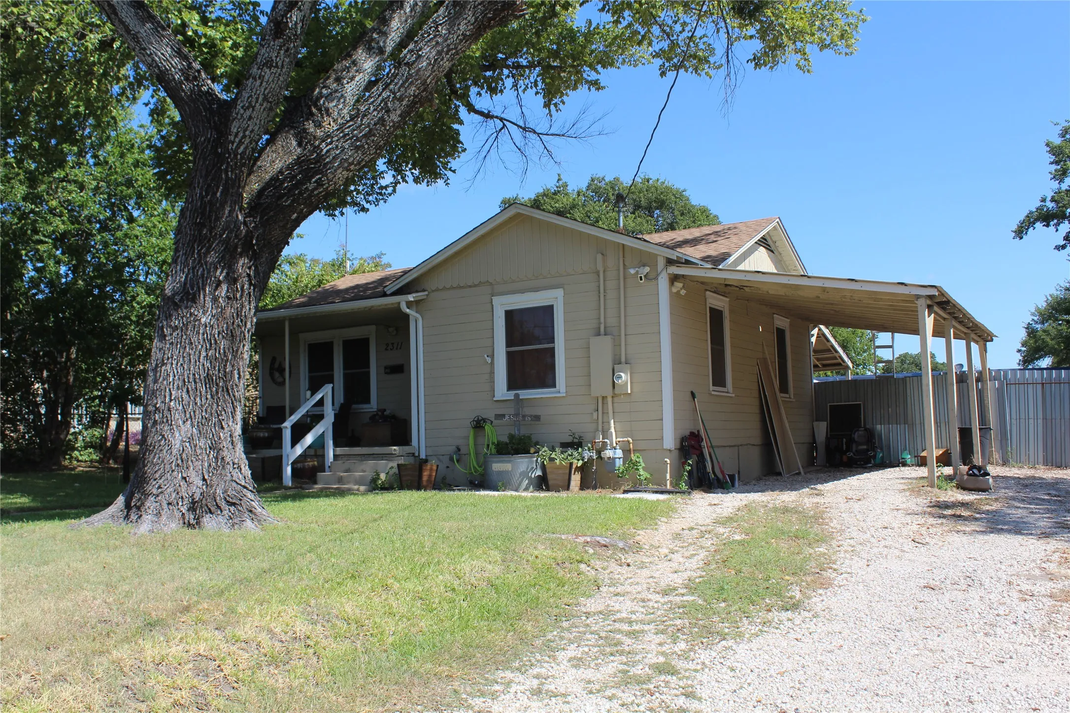 Single-story residence with a covered front porch, gravel driveway, and a side carport structure
