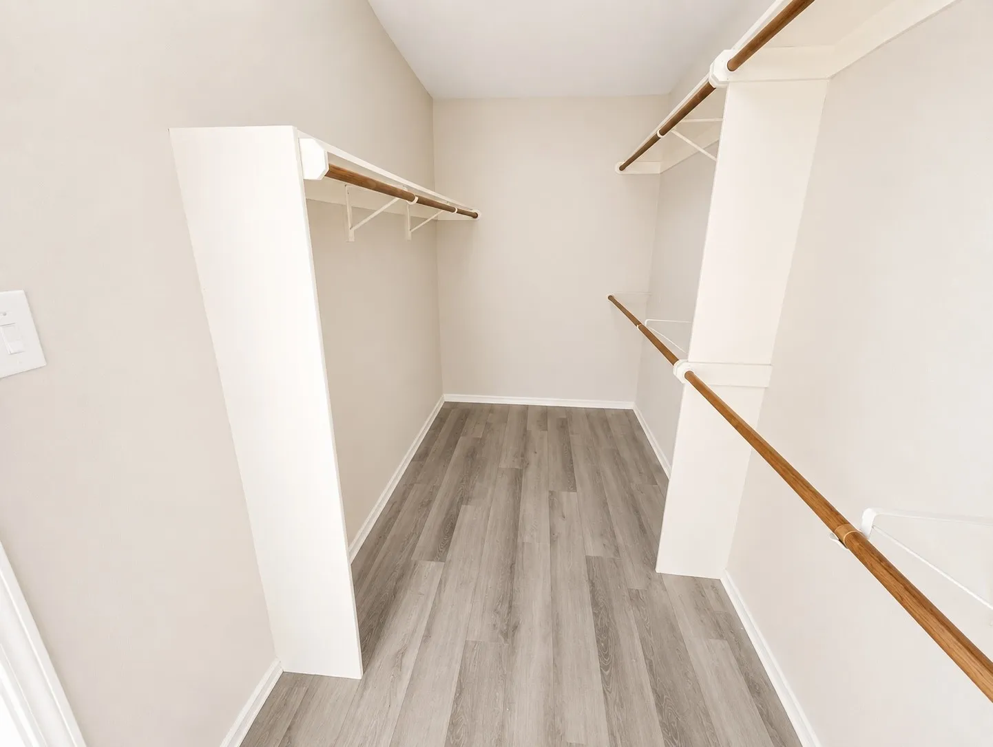 Walk-in closet featuring wood-finish flooring, white walls, and built-in shelving with hanging rods