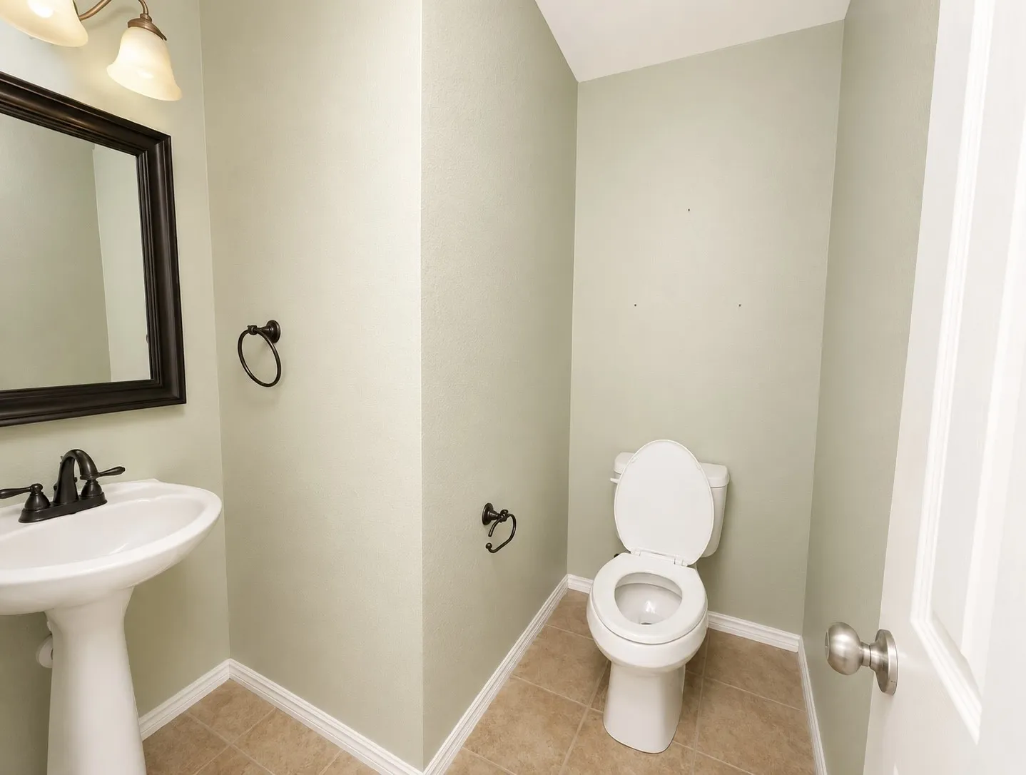 Pedestal sink with dark bronze faucet, framed mirror, and tile flooring
