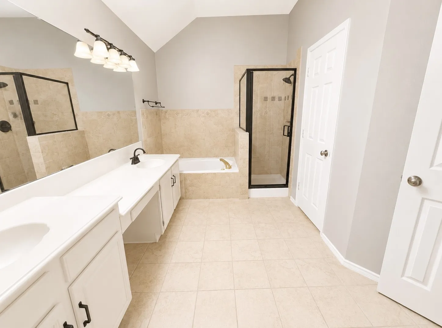 Dual vanities with integrated sinks, a built-in tub, separate shower with glass enclosure, tile flooring, and a vaulted ceiling