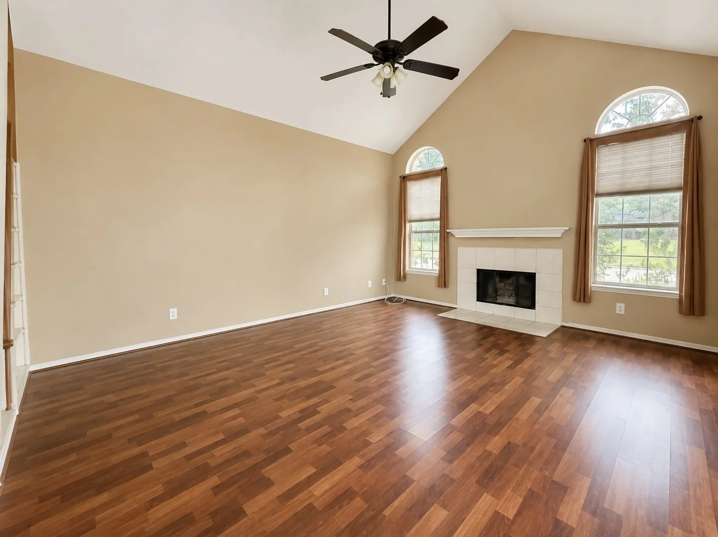Vaulted ceiling featuring a ceiling fan, wood-finish flooring, fireplace with a tile surround and mantel, and arched windows