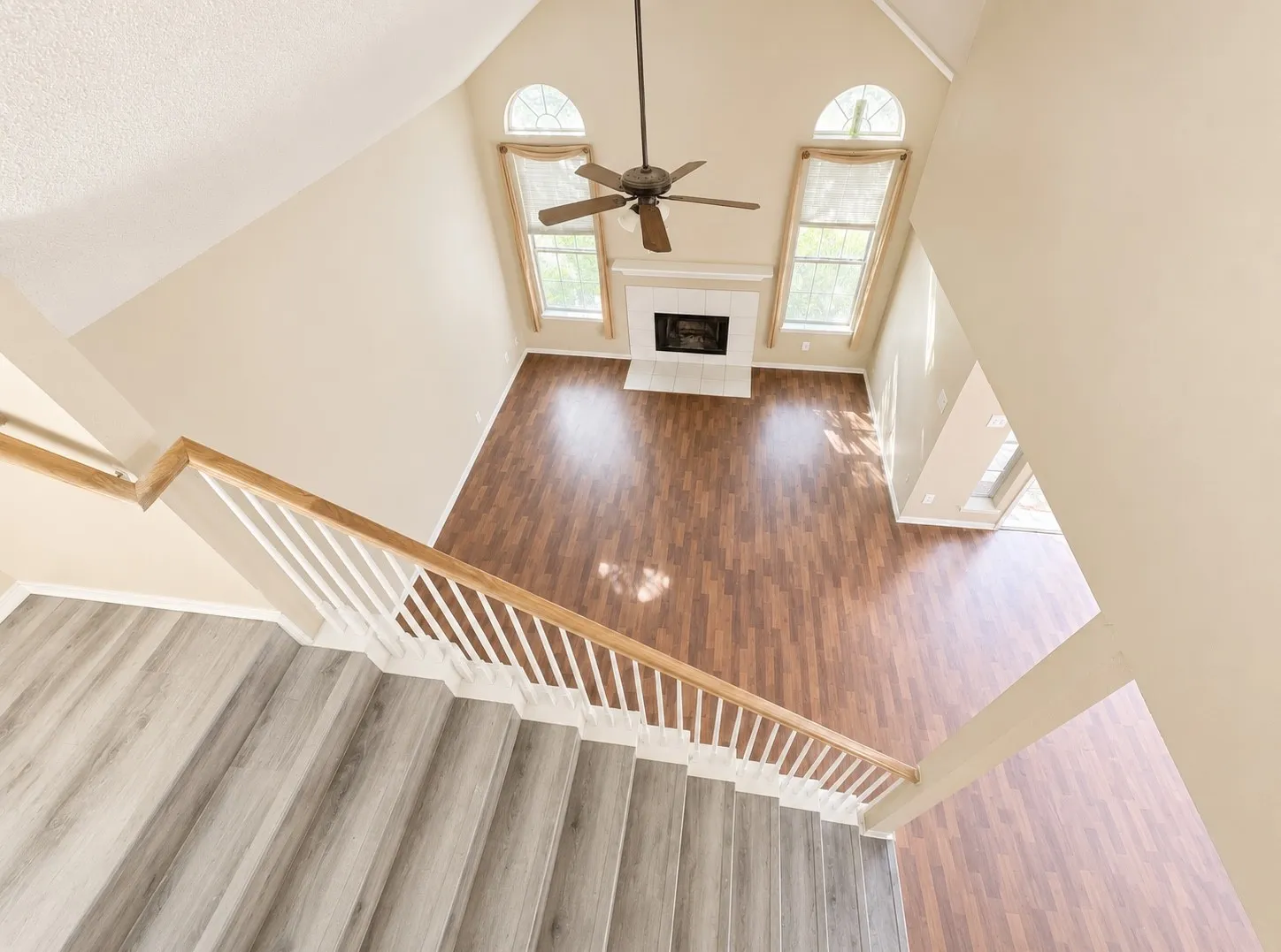 Two-story living area with vaulted ceiling, fireplace, wood-finish flooring, and arched windows