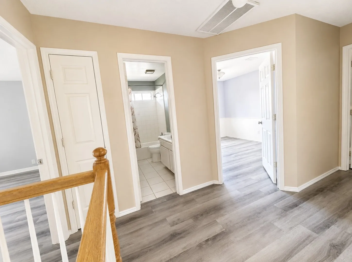 Wood-finish flooring throughout, featuring a light wood banister, white trim, and neutral wall tones