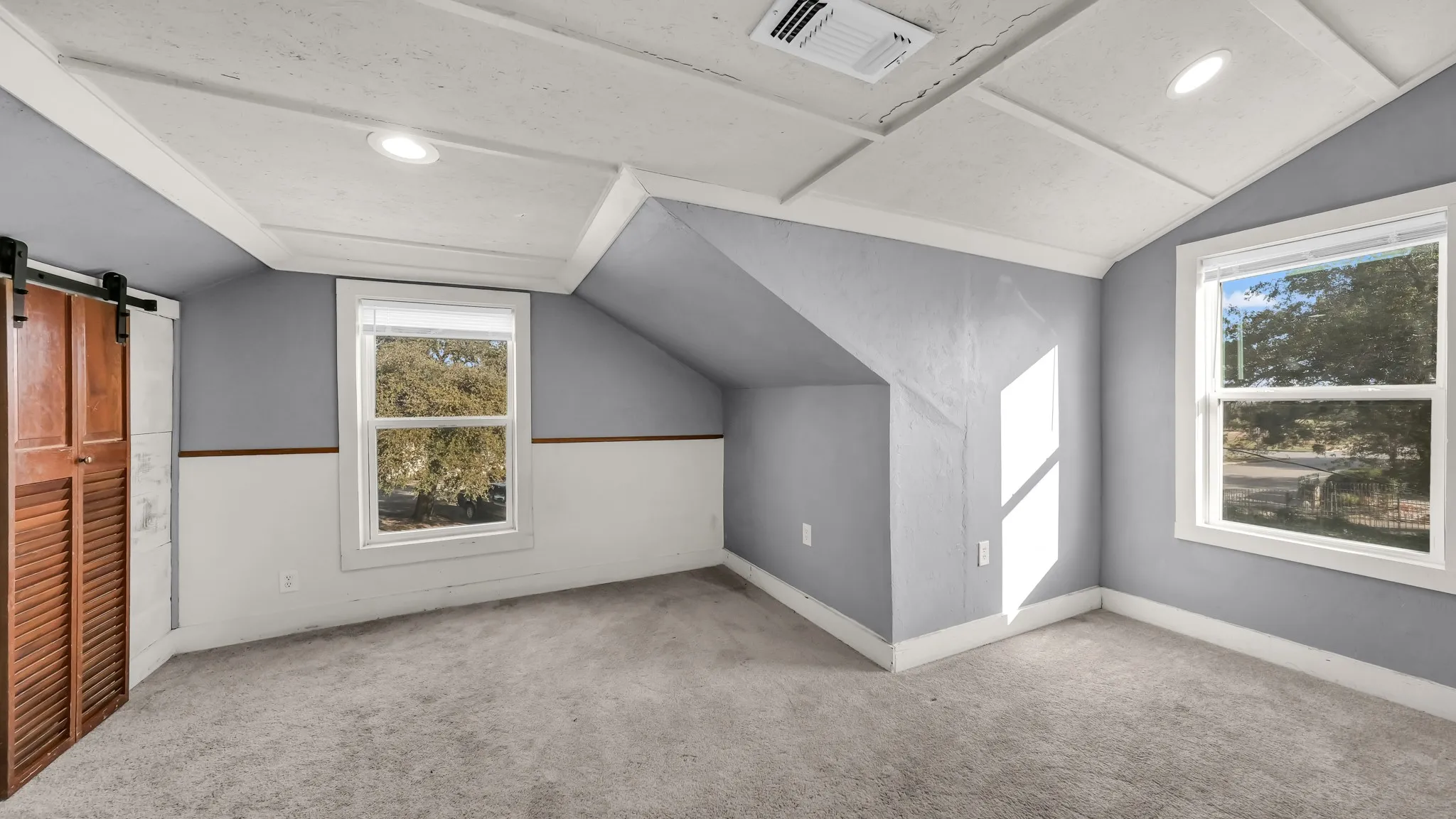 Sloped ceiling with recessed lighting, two windows, carpeted flooring, and a barn door closet