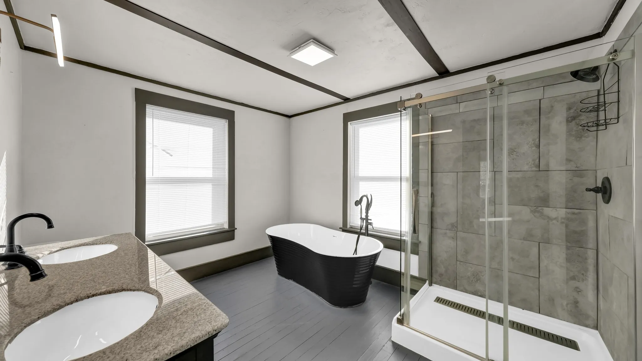 Bathroom featuring a dual vanity with stone-finish countertop, black freestanding soaking tub, and a shower with sliding glass door and tile surround