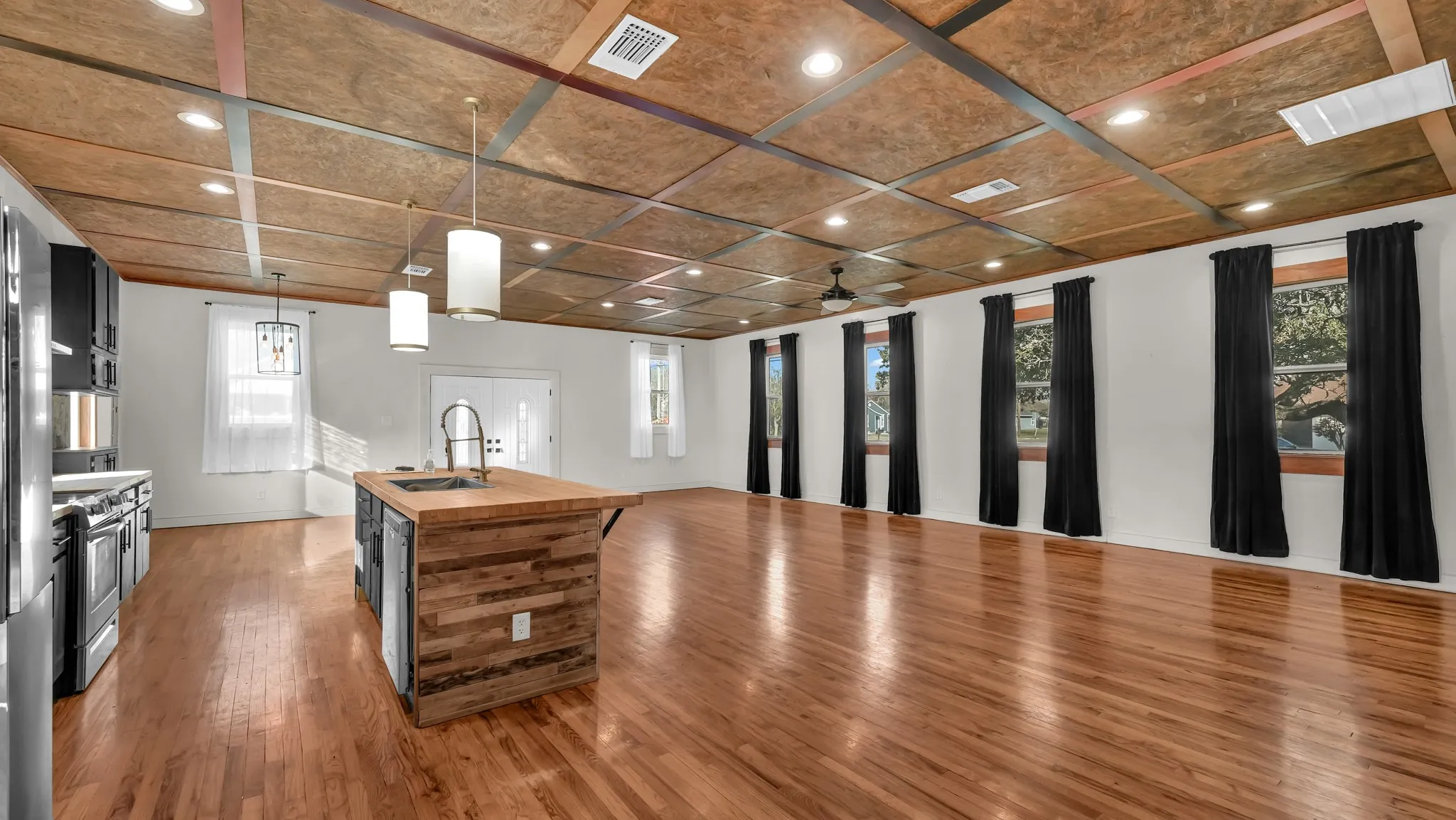Open-concept living space featuring wood-finish flooring, a wood-clad kitchen island, recessed lighting, and multiple windows