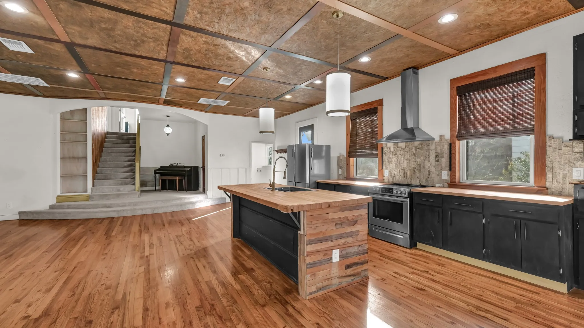 Hardwood flooring, kitchen island with wood-finish counter, black cabinetry, stainless steel appliances, and a coffered ceiling