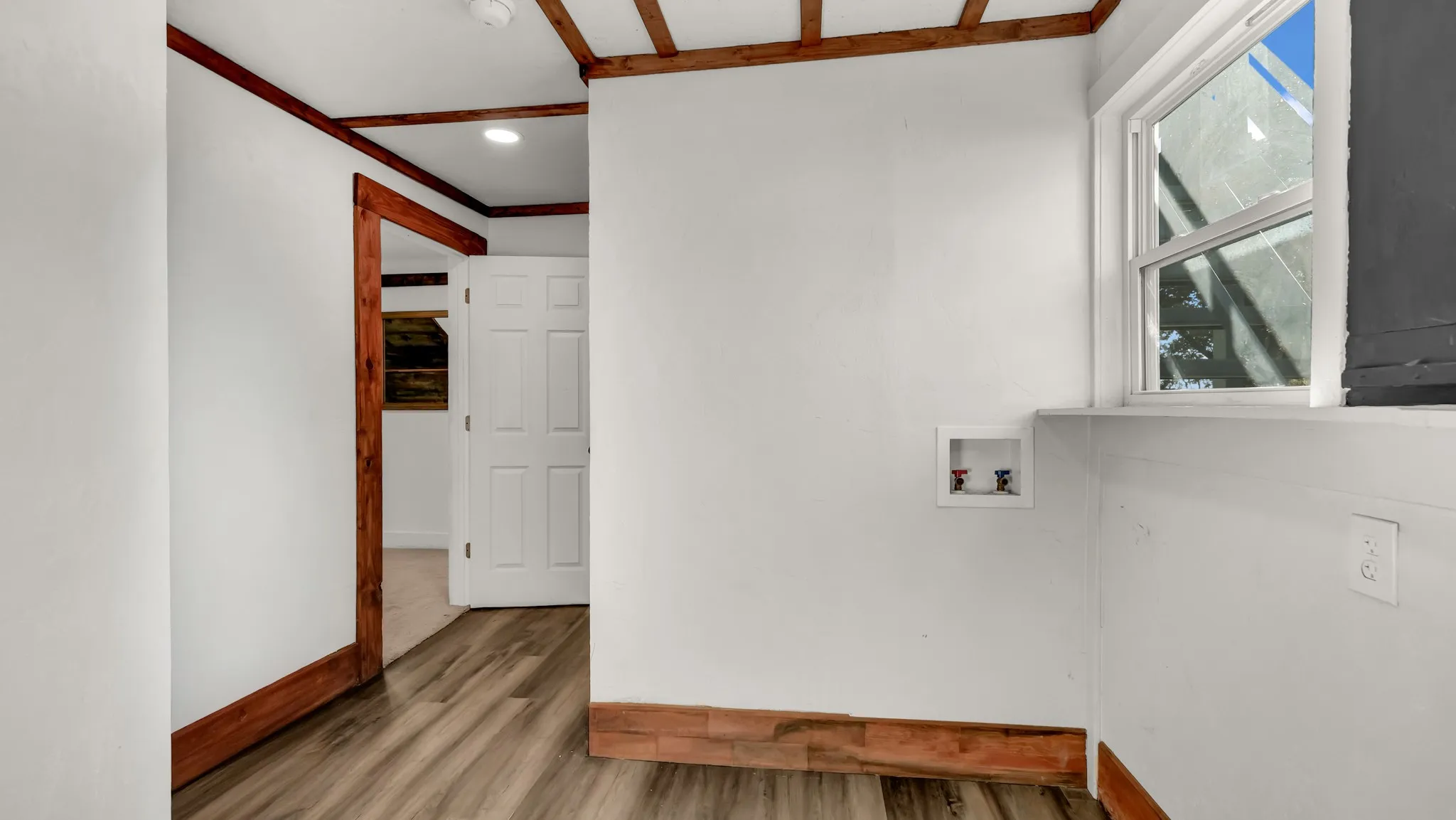 Wood-finish flooring, wood trim accents, a paneled door, ceiling beams, and a window for natural light