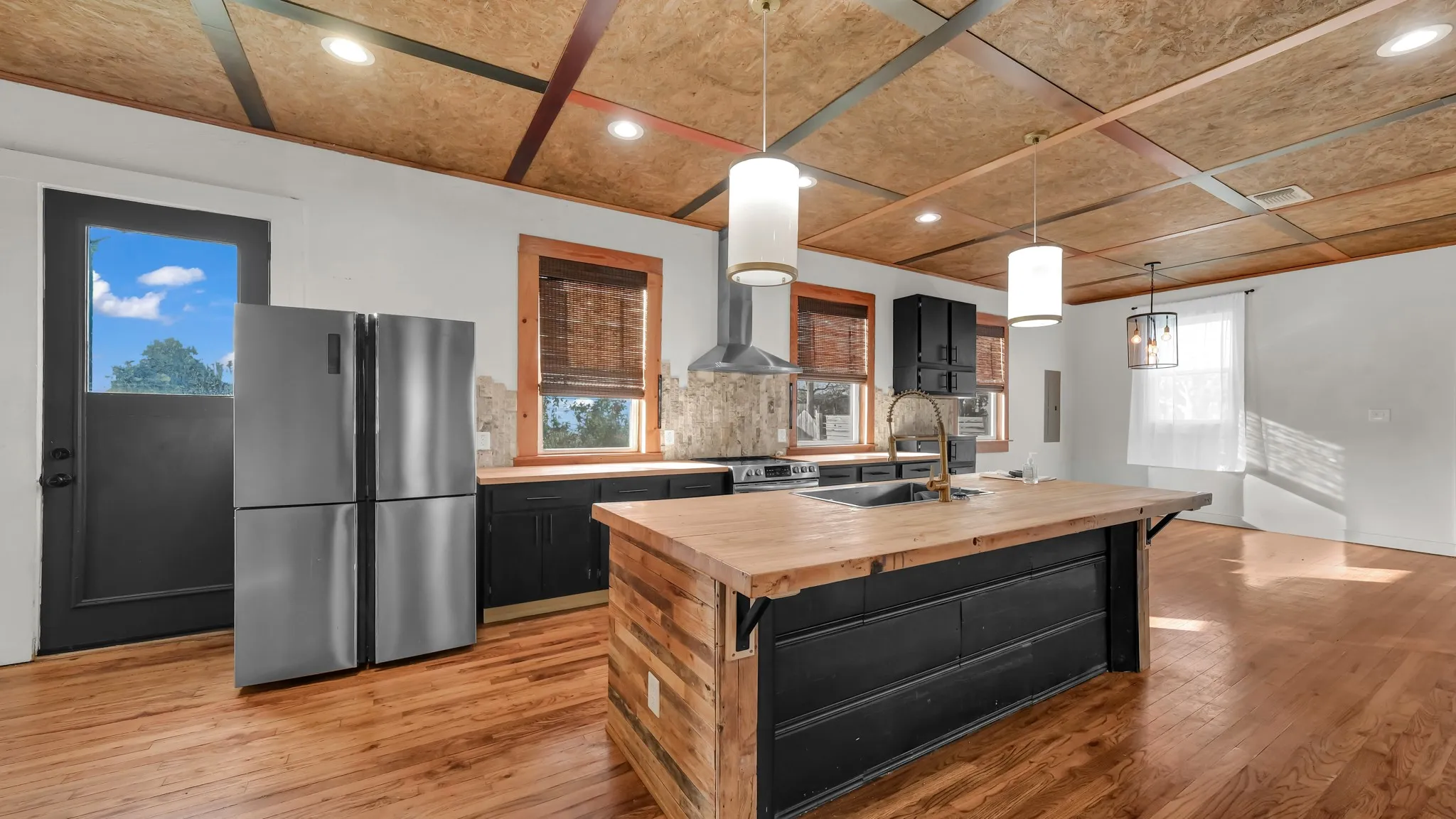 Open-concept kitchen featuring an oversized island with wood countertop, built-in cabinetry, stainless steel appliances, and wood-finish flooring