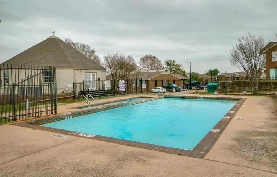 Rectangular swimming pool with surrounding concrete decking, secured by a wrought iron fence