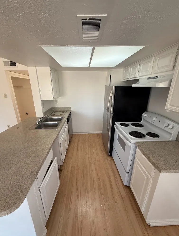 Galley kitchen with wood-finish flooring, white cabinetry, integrated double basin sink, and a black and stainless steel refrigerator