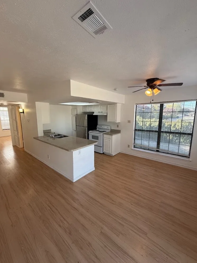 Open concept living space featuring wood-finish flooring, white cabinetry, and stainless steel appliances