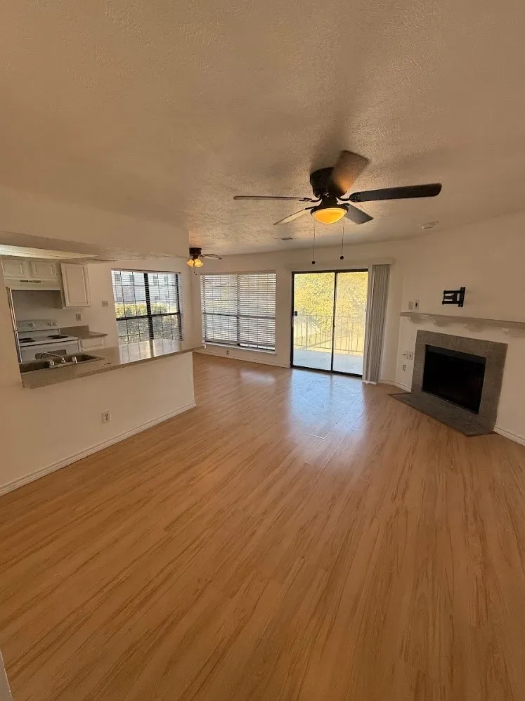 Wood-finish flooring throughout, ceiling fans, and a fireplace with a stone hearth and mantel