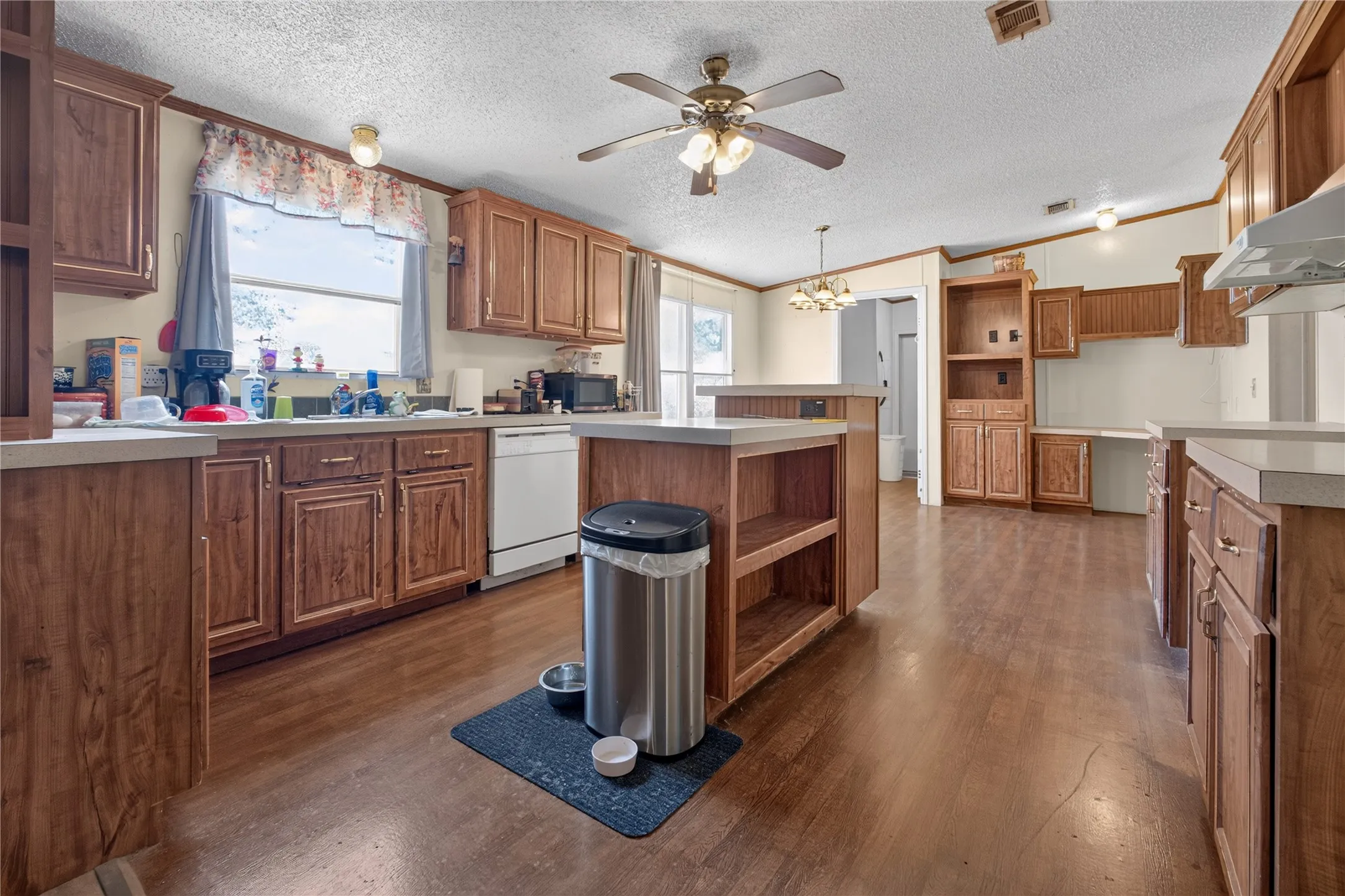 Spacious kitchen featuring wood cabinetry, a center island with seating, stainless steel appliances, wood-finish flooring throughout, and abundant natural light from multiple windows