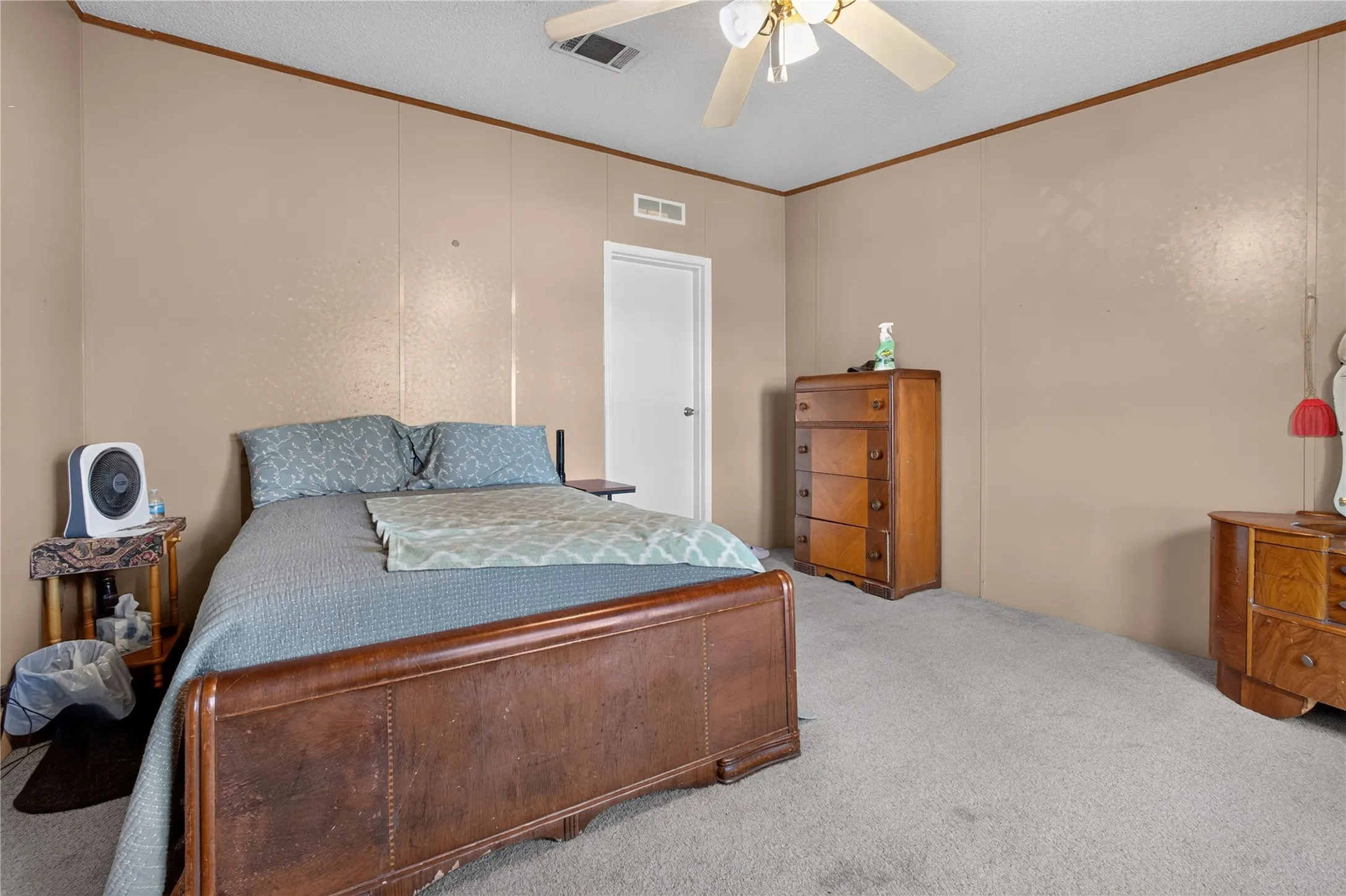 Spacious primary bedroom with warm neutral walls, carpeted flooring, and ceiling fan with integrated lighting