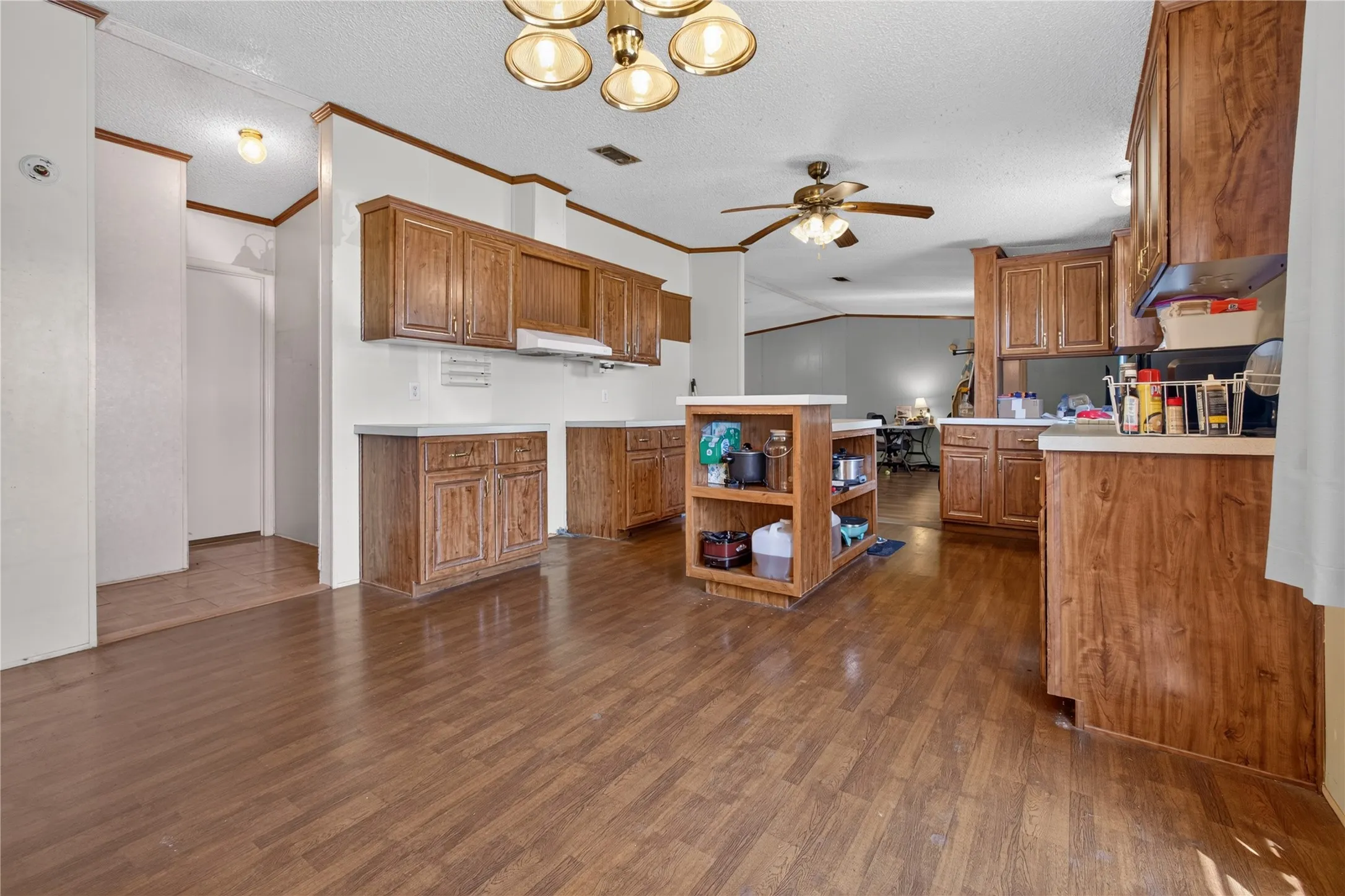 Open-concept kitchen with wood-finish flooring, wood cabinetry, light-toned countertops, and a central island with open shelving