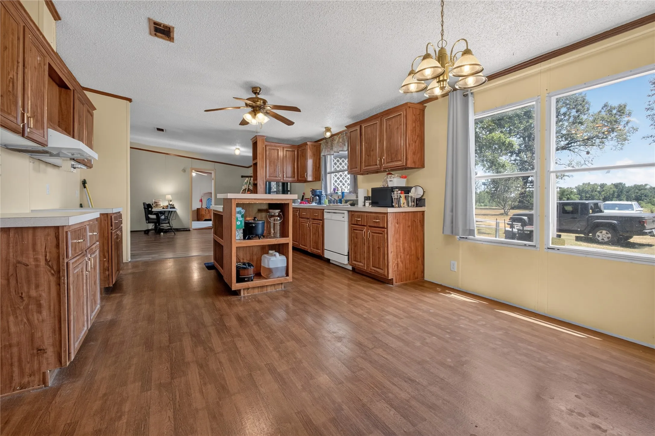 Wood-finish flooring, wood cabinetry with light-toned countertops, a ceiling fan, and multiple windows