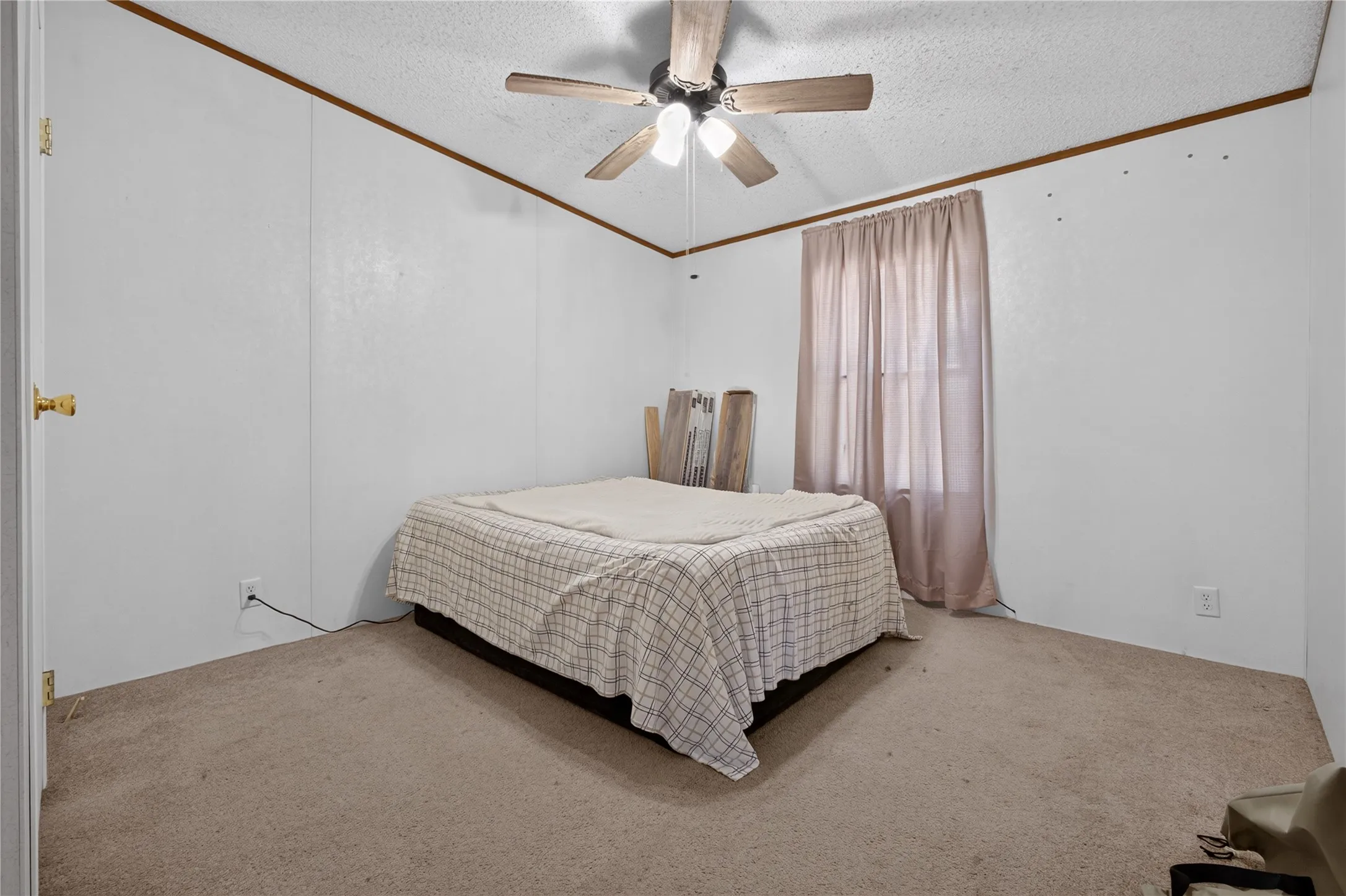 Spacious bedroom with neutral carpet flooring, ceiling fan with integrated lighting, and large window with soft-draped curtains allowing natural light