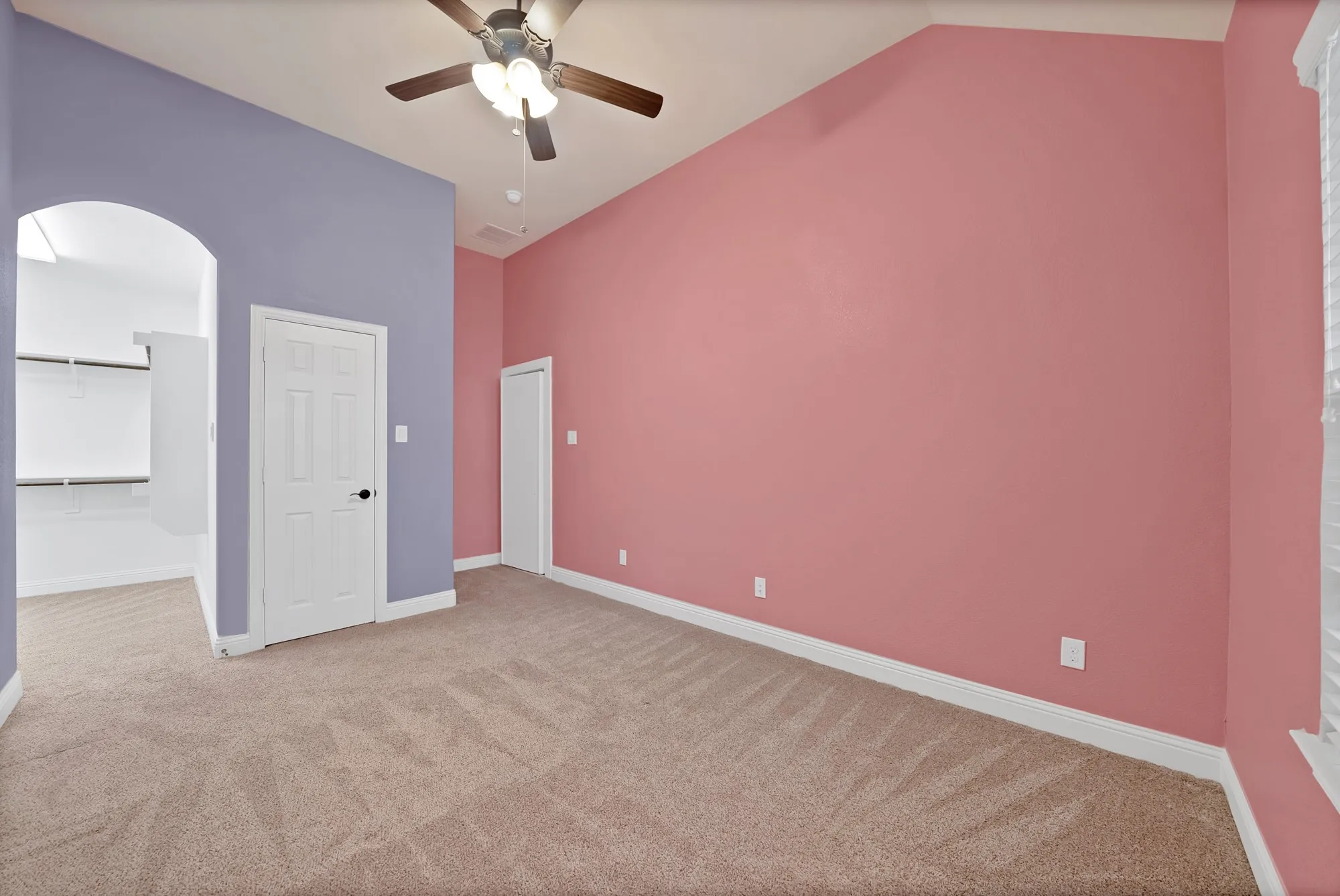 Vaulted ceiling with a ceiling fan light fixture, carpeted flooring, and an arched entryway leading to a walk-in closet with built-in shelving