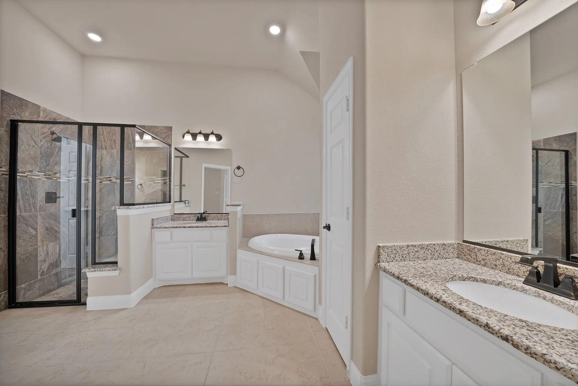 Spacious bathroom featuring a built-in soaking tub, dual vanity with granite countertops, and a walk-in shower with tiled walls and a glass enclosure