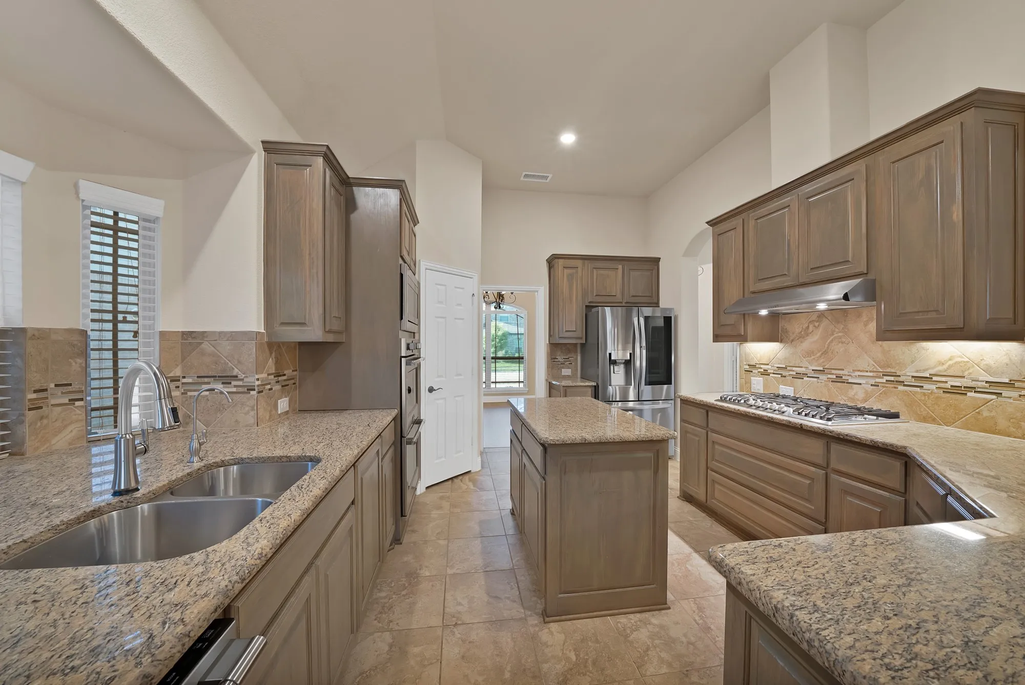 Kitchen featuring wood cabinetry, a stainless steel double basin sink, stainless steel appliances, an island, and tile flooring