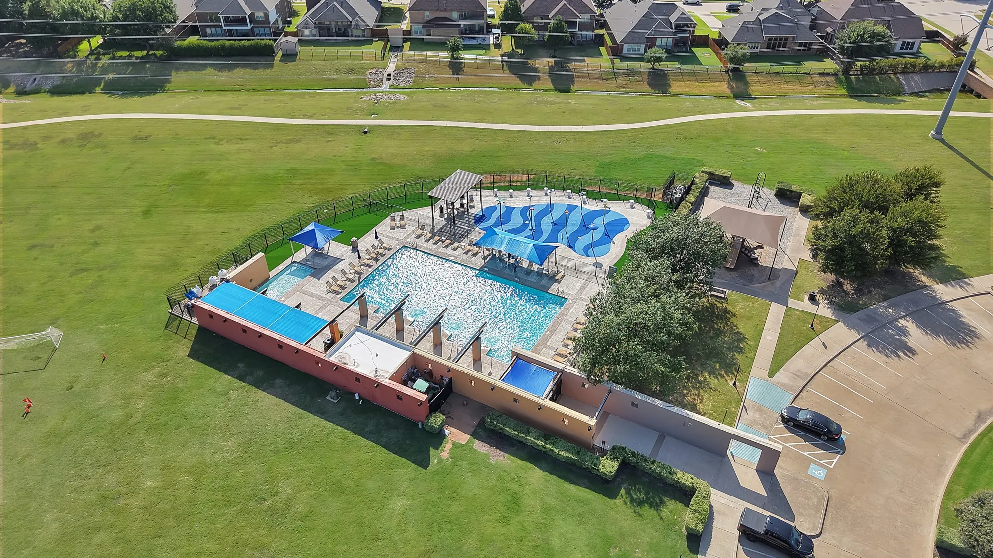 Community pool with a separate shallow wading pool, adjacent to a playground and expansive green space