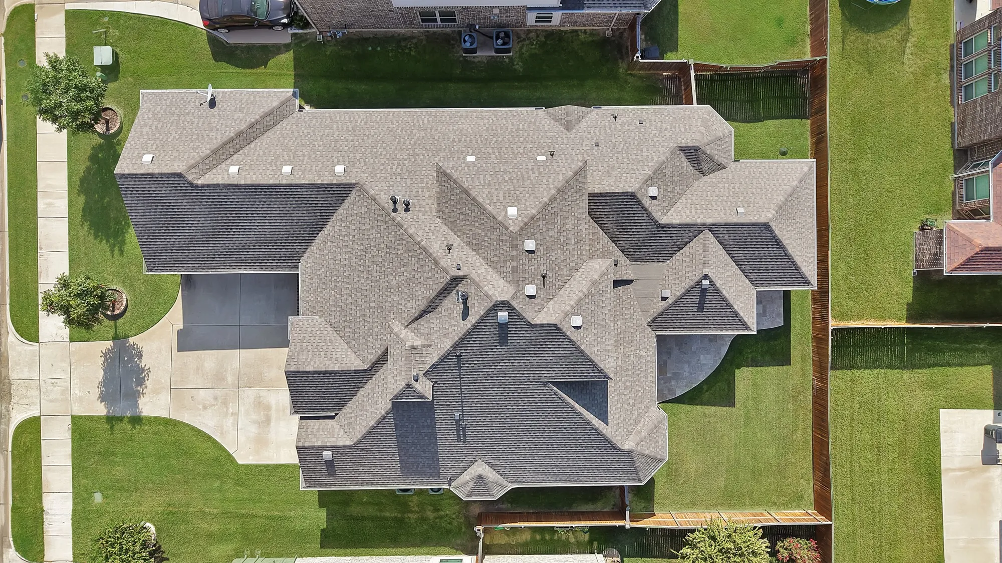 Expansive asphalt shingle roofline, concrete driveway, and a large grass lawn