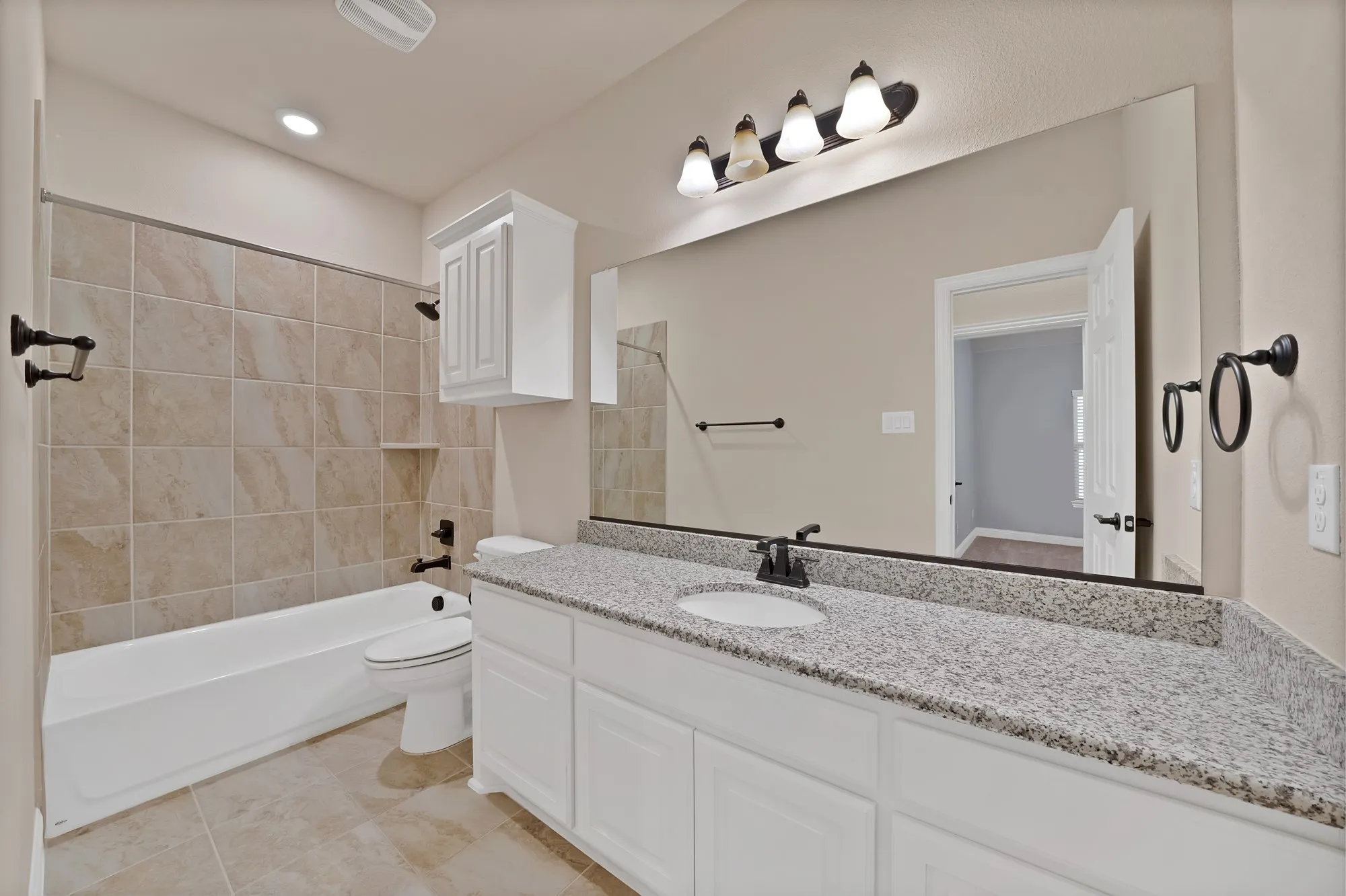 Full-sized mirror, recessed lighting, tile flooring, tile shower surround, and a vanity with a stone countertop