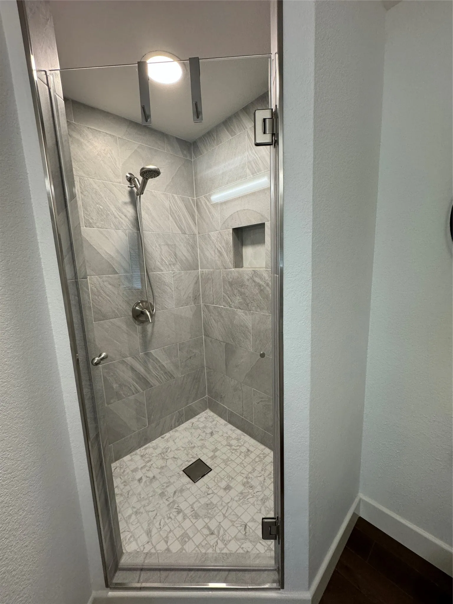 Glass-enclosed shower with gray tiled walls and a recessed niche