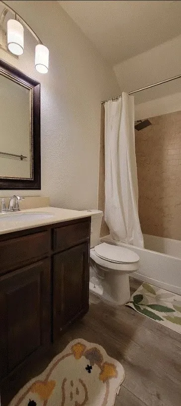 Wood-finish flooring with a dark wood vanity, light-colored countertop, and a tiled shower surround