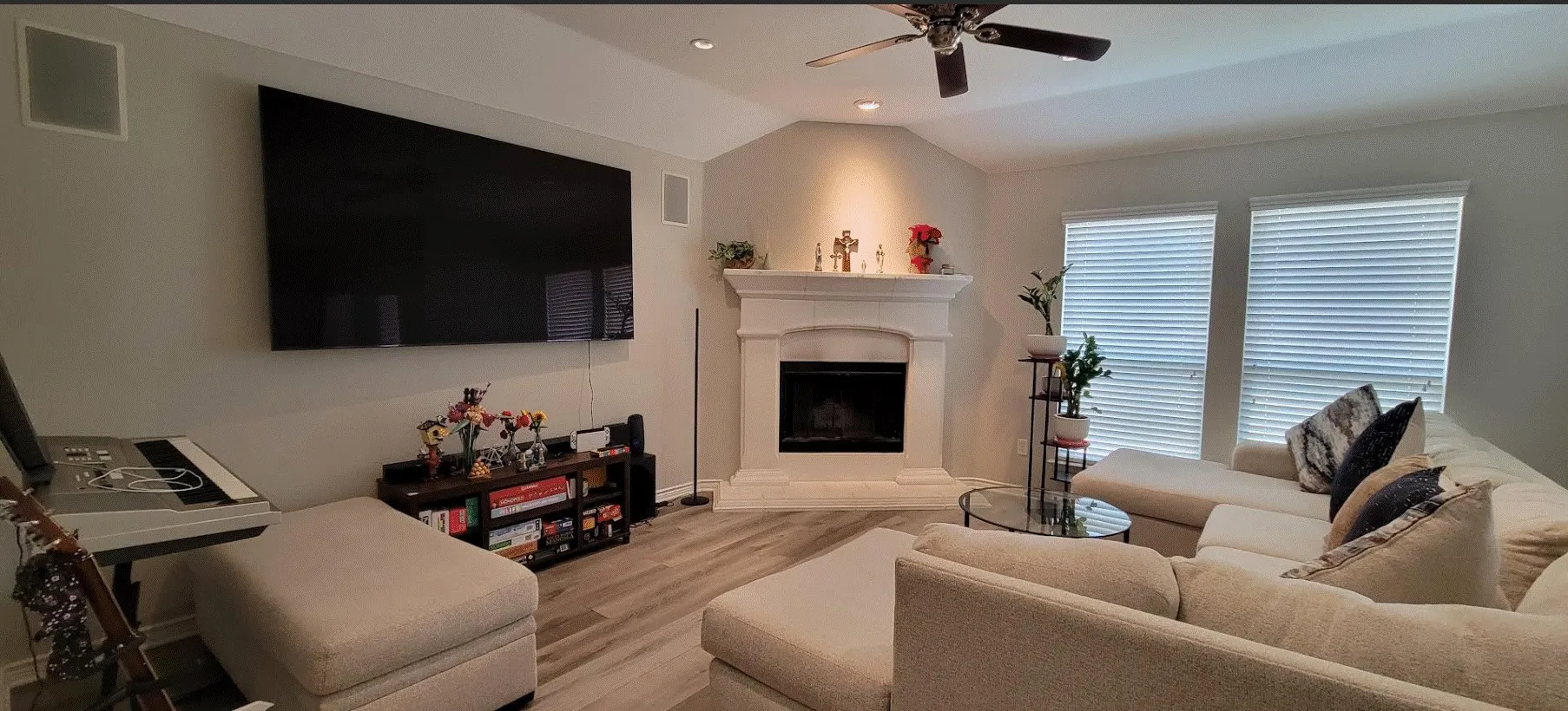 Vaulted ceiling with recessed lighting and ceiling fan, electric fireplace with white mantel, wood-finish flooring, and dual windows with blinds