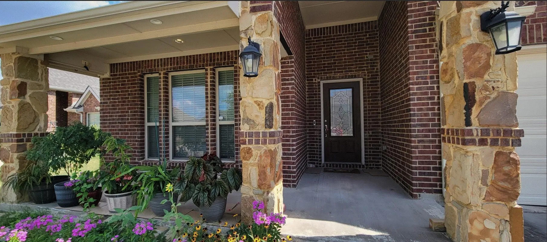 Brick exterior with stone columns, covered porch, recessed lighting, and a front entry door with decorative glass