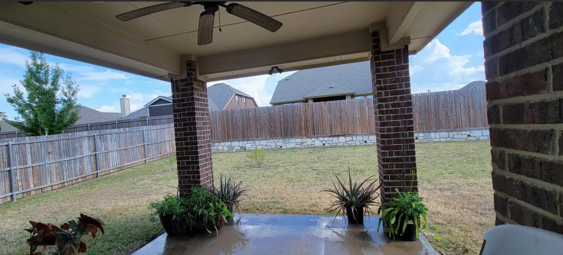 Covered patio with brick pillars, concrete flooring, and a ceiling fan